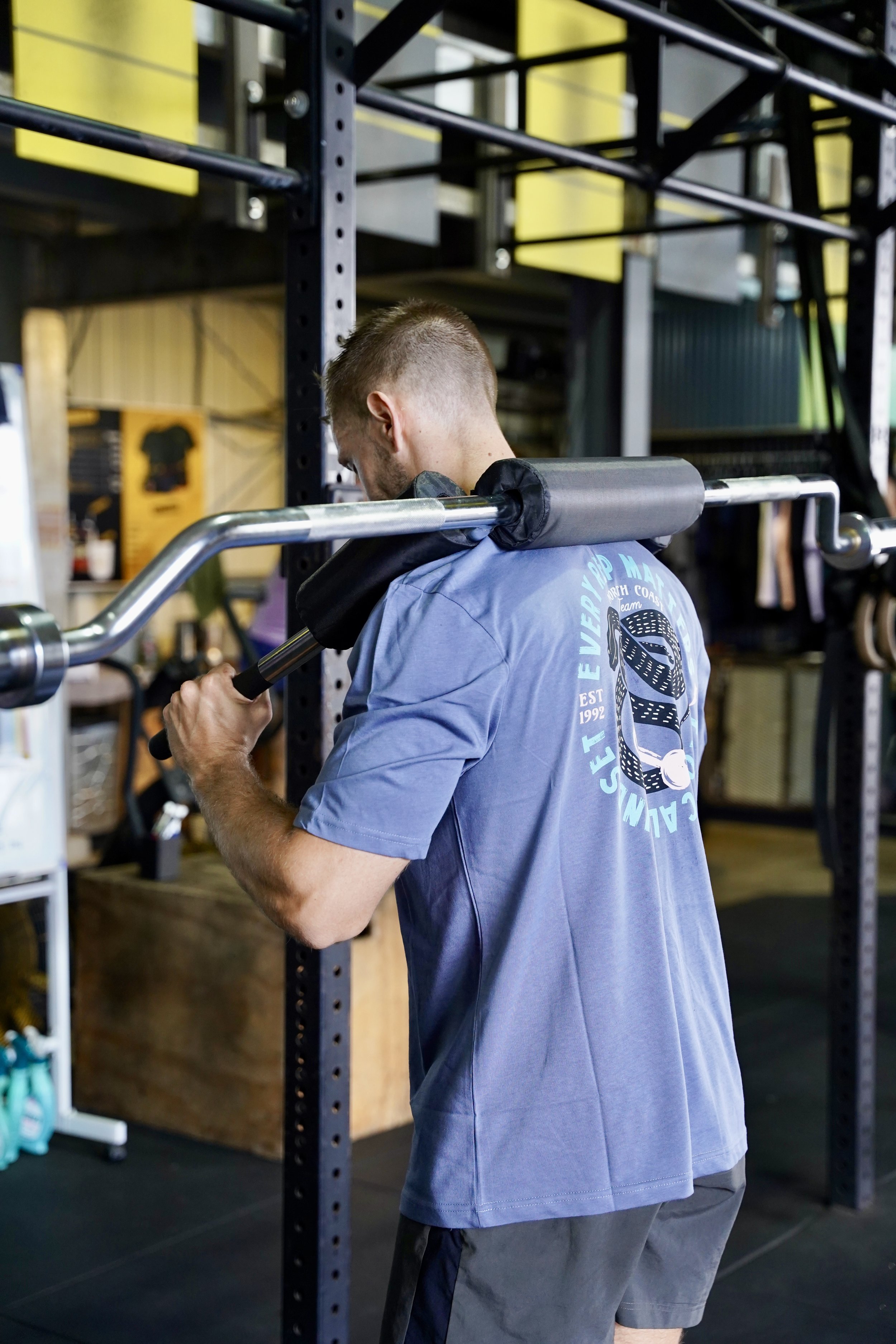 L’image montre un homme faisant un squat et habillé d’un t-shirt bleu
