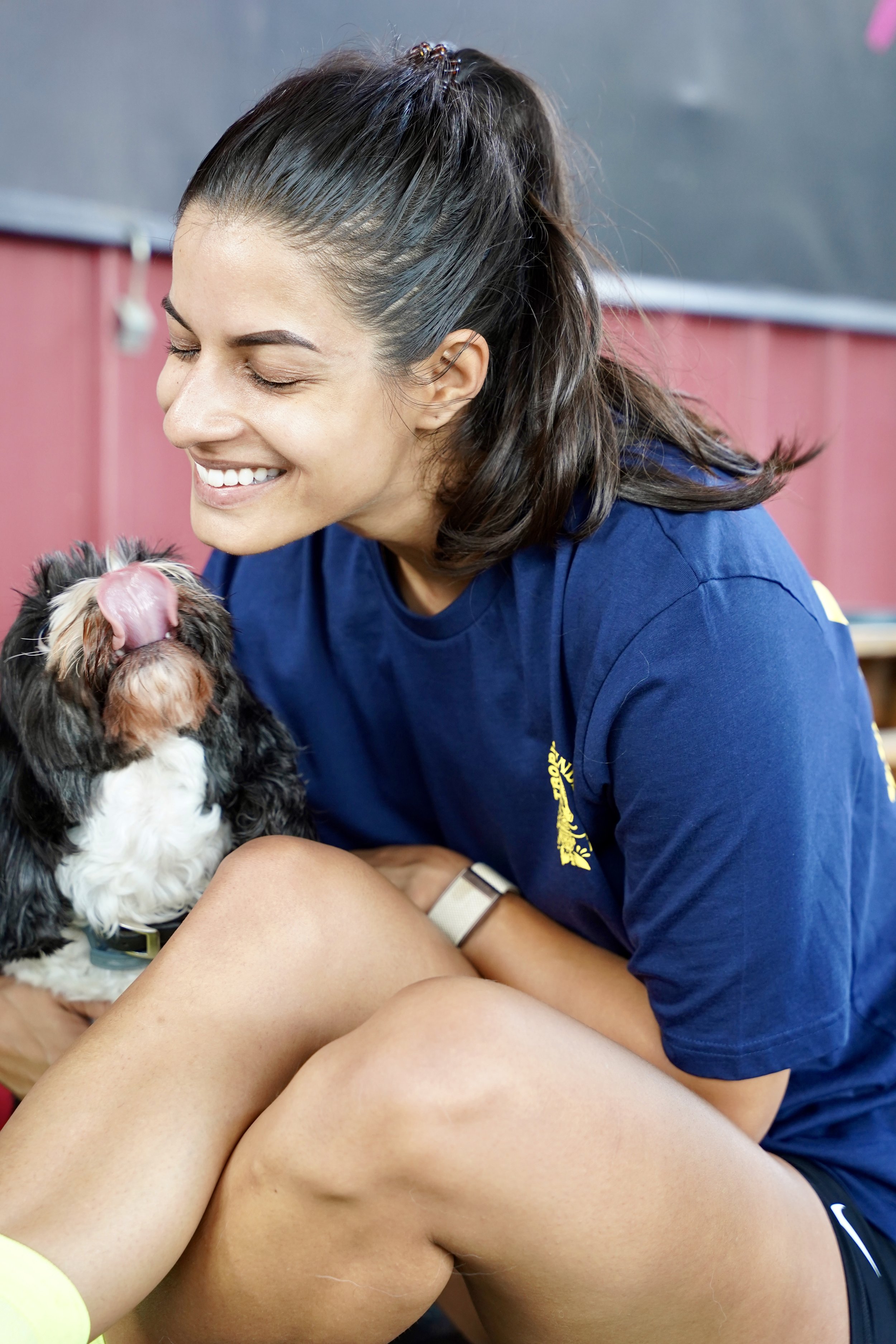 L’image montre une femme heureuse avec un chien. Elle est vêtue d’un t-shirt bleu avec un logo jaune sur la poitrine
