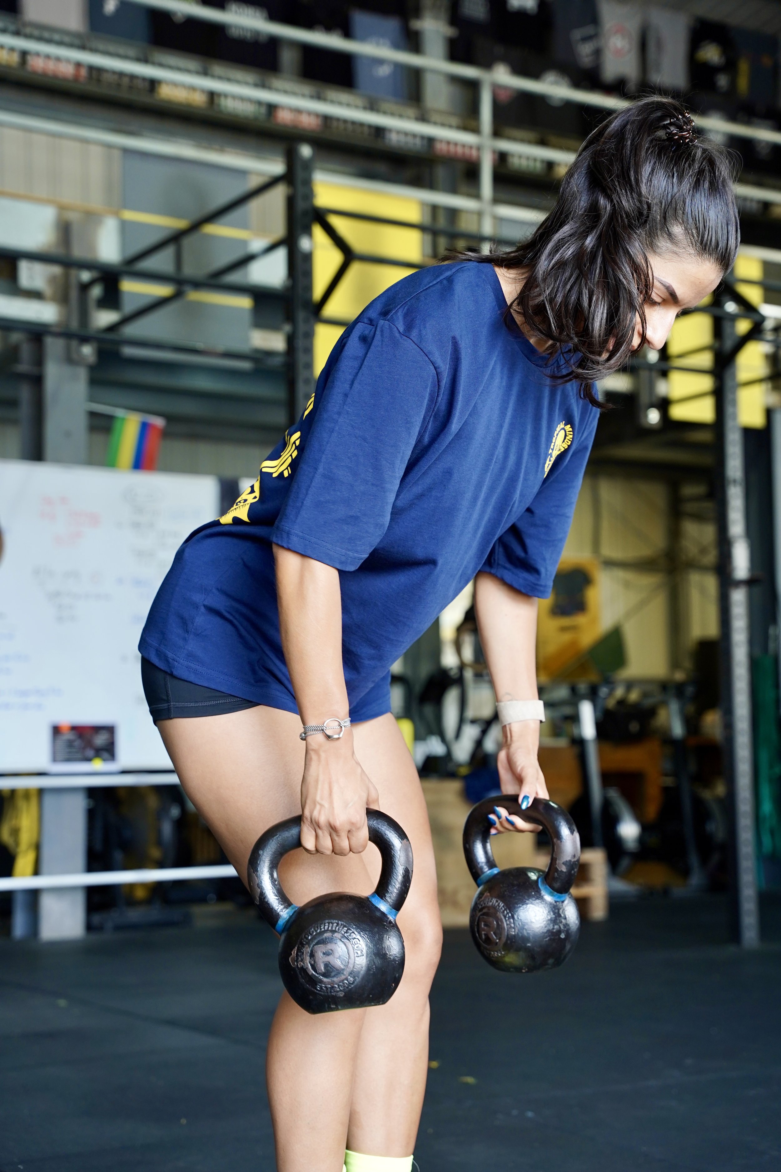 L’image montre une femme faisant du CrossFit vêtue d’un t-shirt bleu avec un logo de tête de mort jaune sur la poitrine
