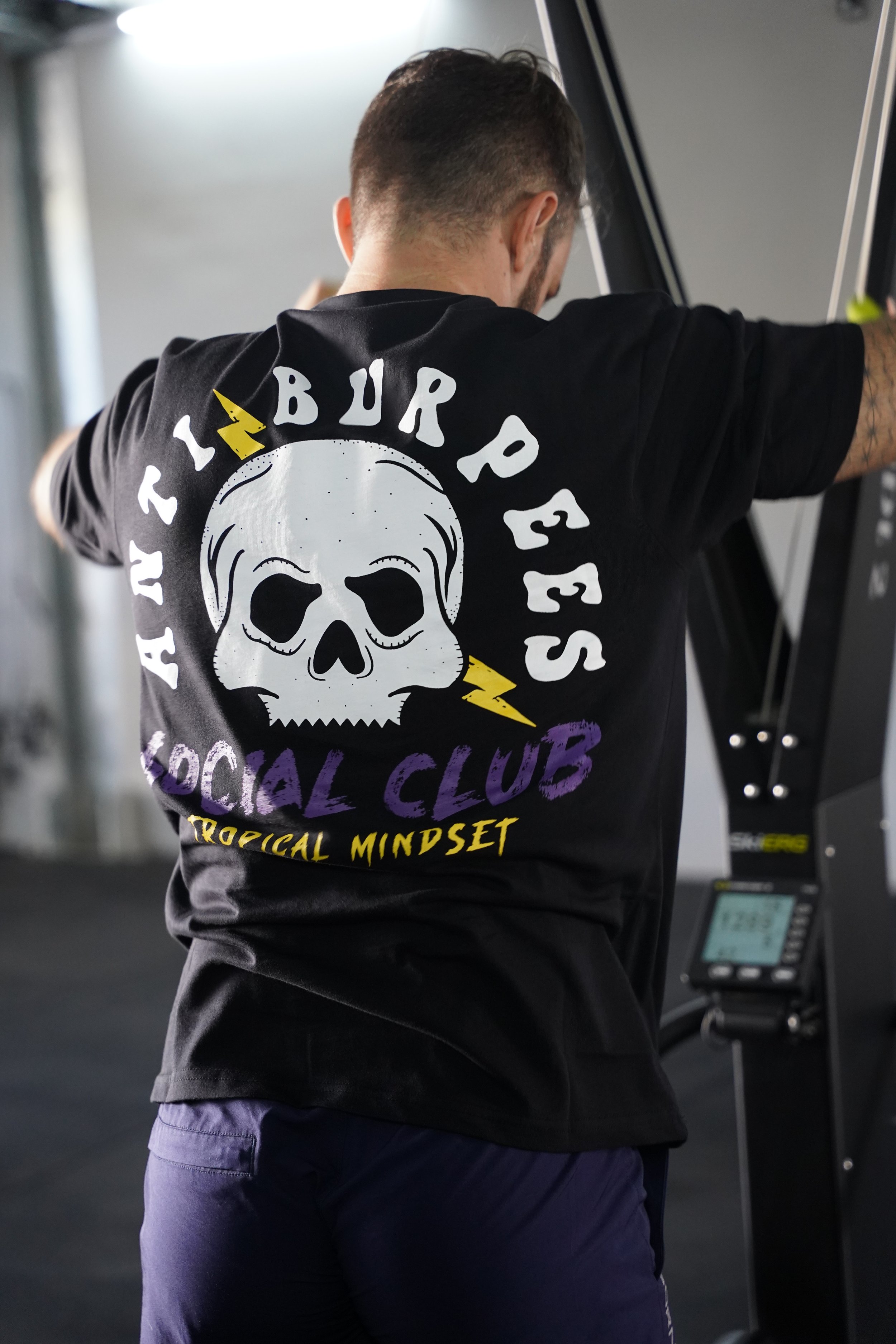 L’image montre un t-shirt avec une tête de mort oú il est noté anti burpees social club. Homme faisant du sport