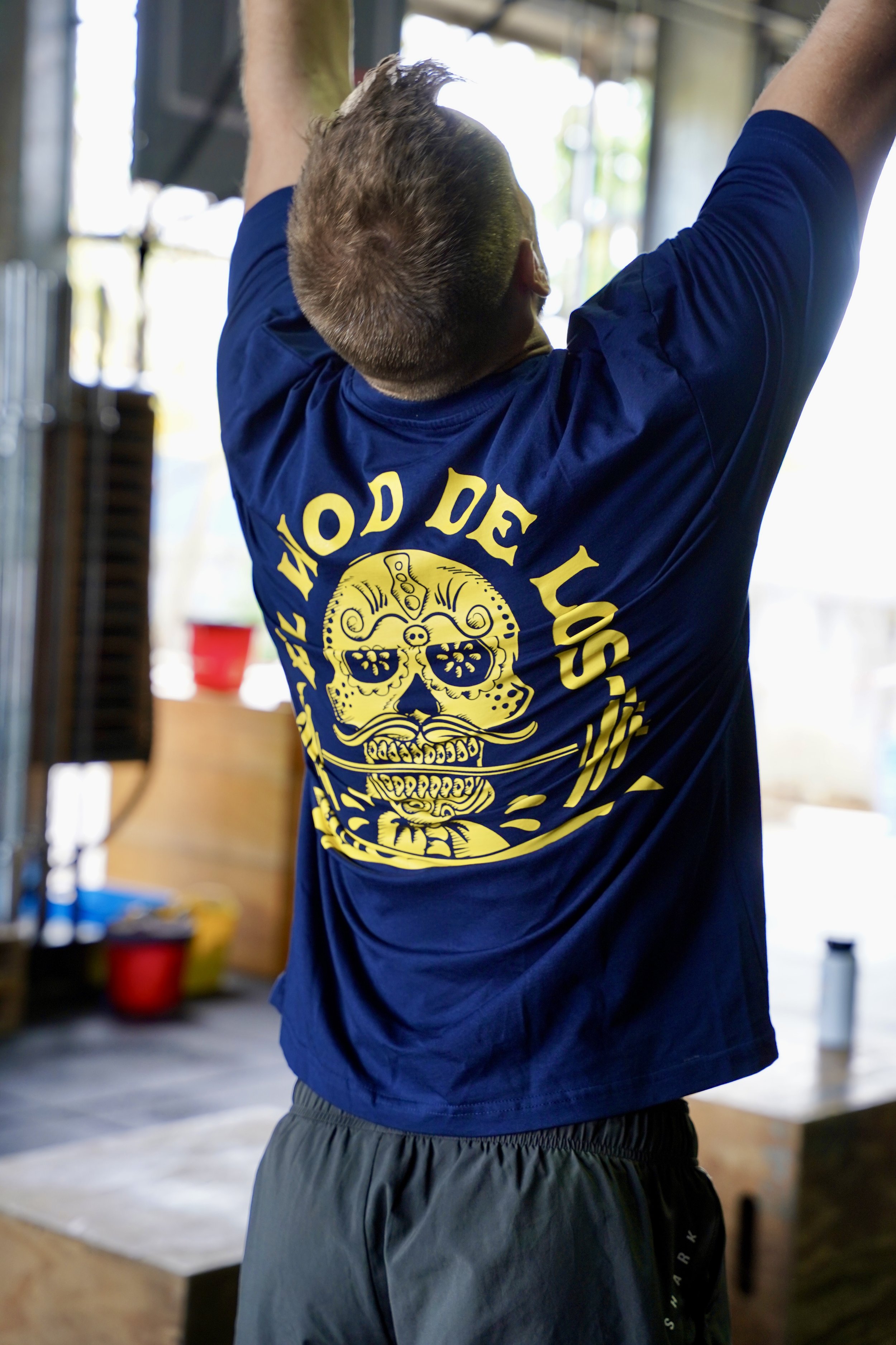 L’image montre un homme faisant du sport et vêtu d’un t-shirt bleu foncé sur lequel on peut voir el wod de los muertos