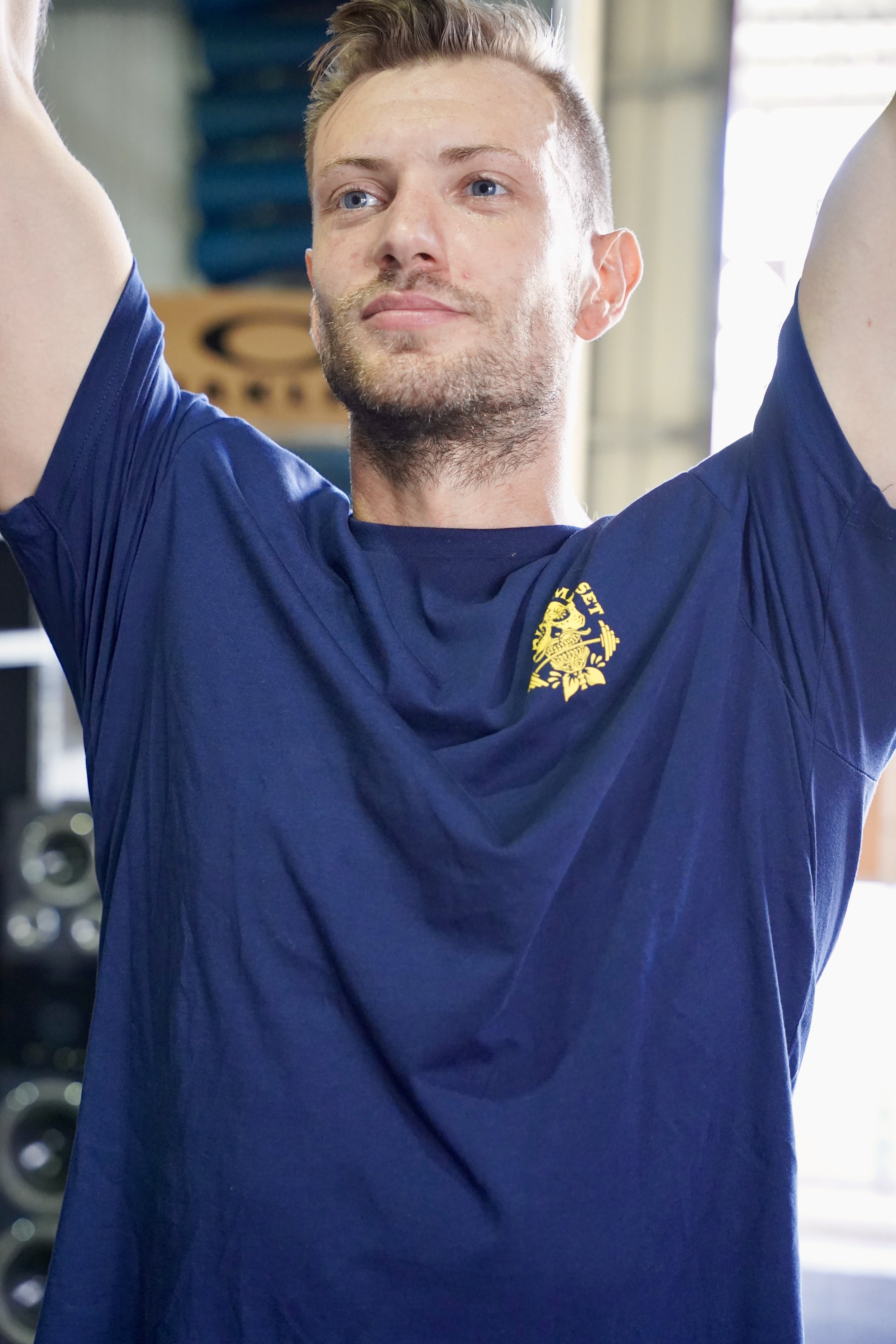 L’image montre un homme vêtu d’un t-shirt bleu foncé avec un logo sur la poitrine