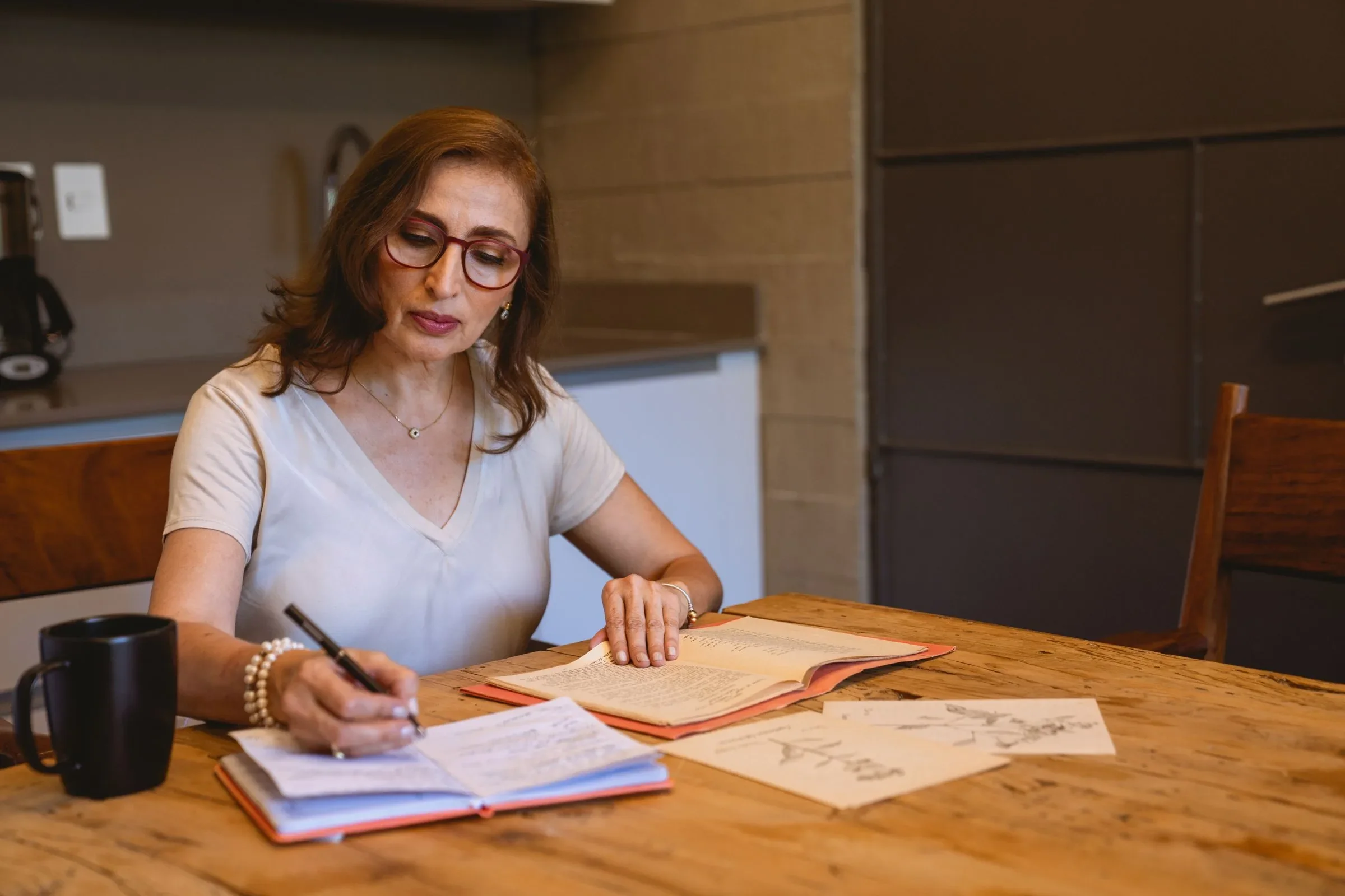 Donna che scrive su un quaderno a un tavolo di legno, come in un diario dei sintomi della menopausa.