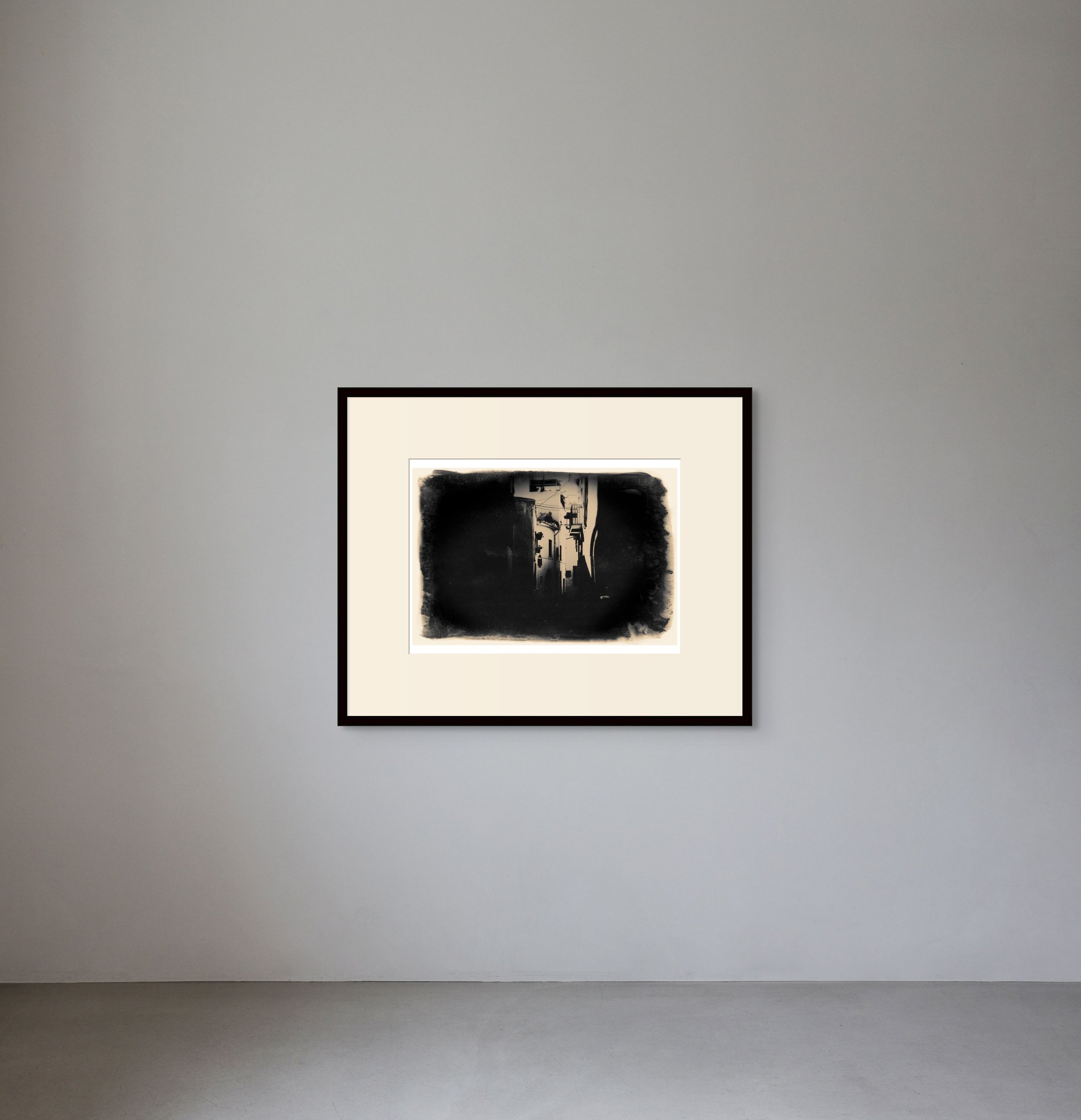 An abstract black and white artwork hanging on a plain gray wall in a minimalist gallery setting.