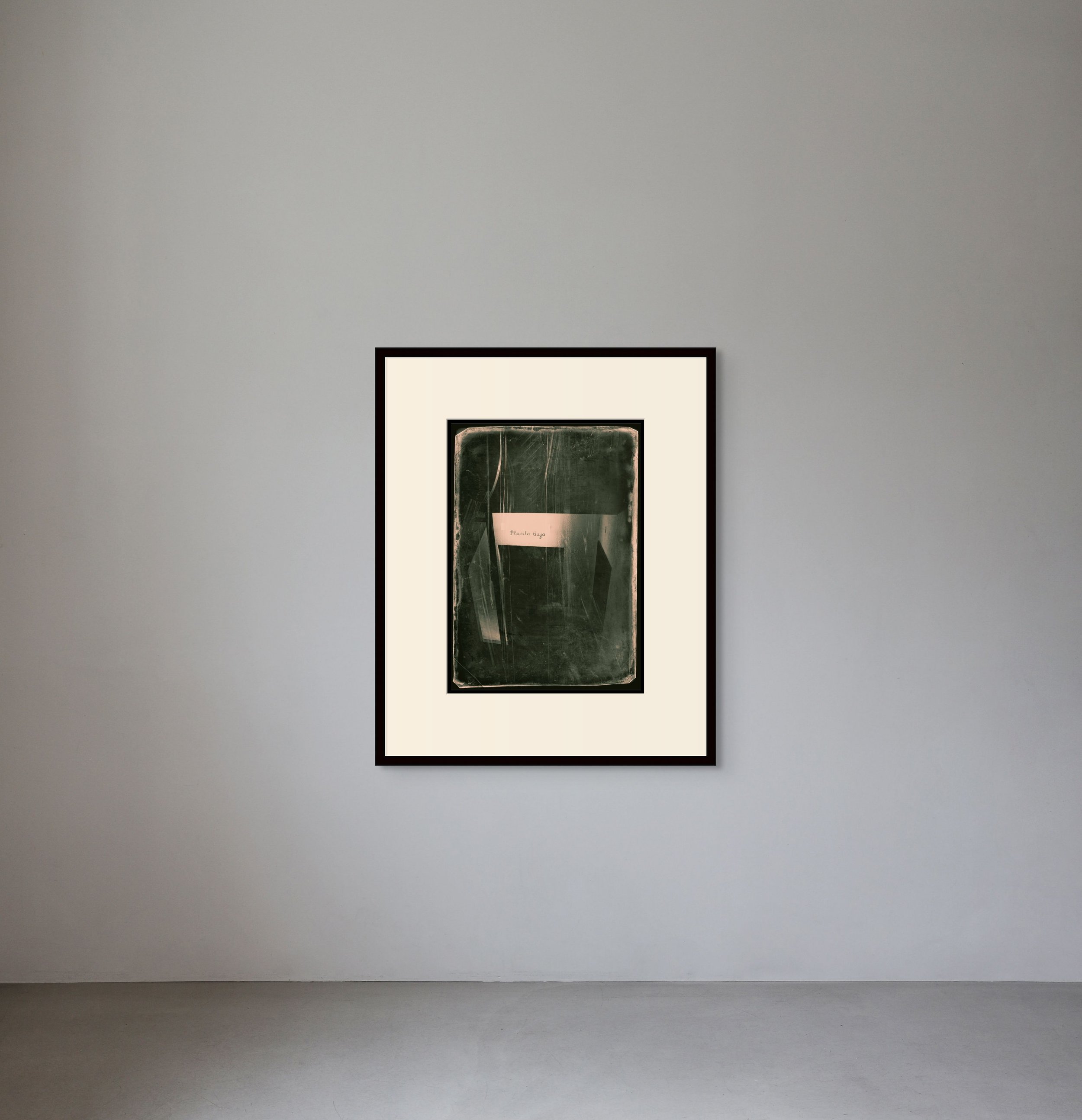 A framed abstract art piece hanging on a plain gray wall in a gallery setting.