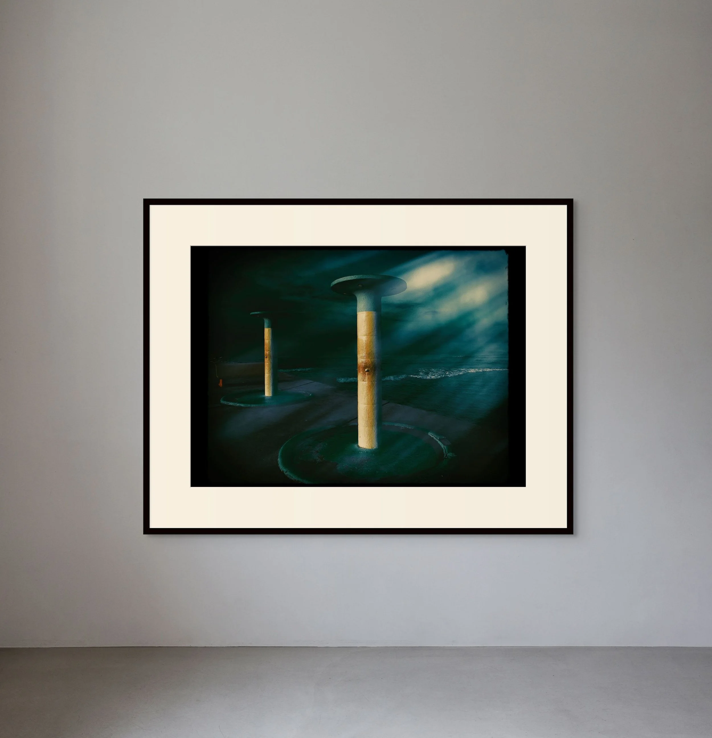 A framed artwork depicting three abstract pillar-like structures with circular tops, set against a dark, moody background with light and shadow effects.