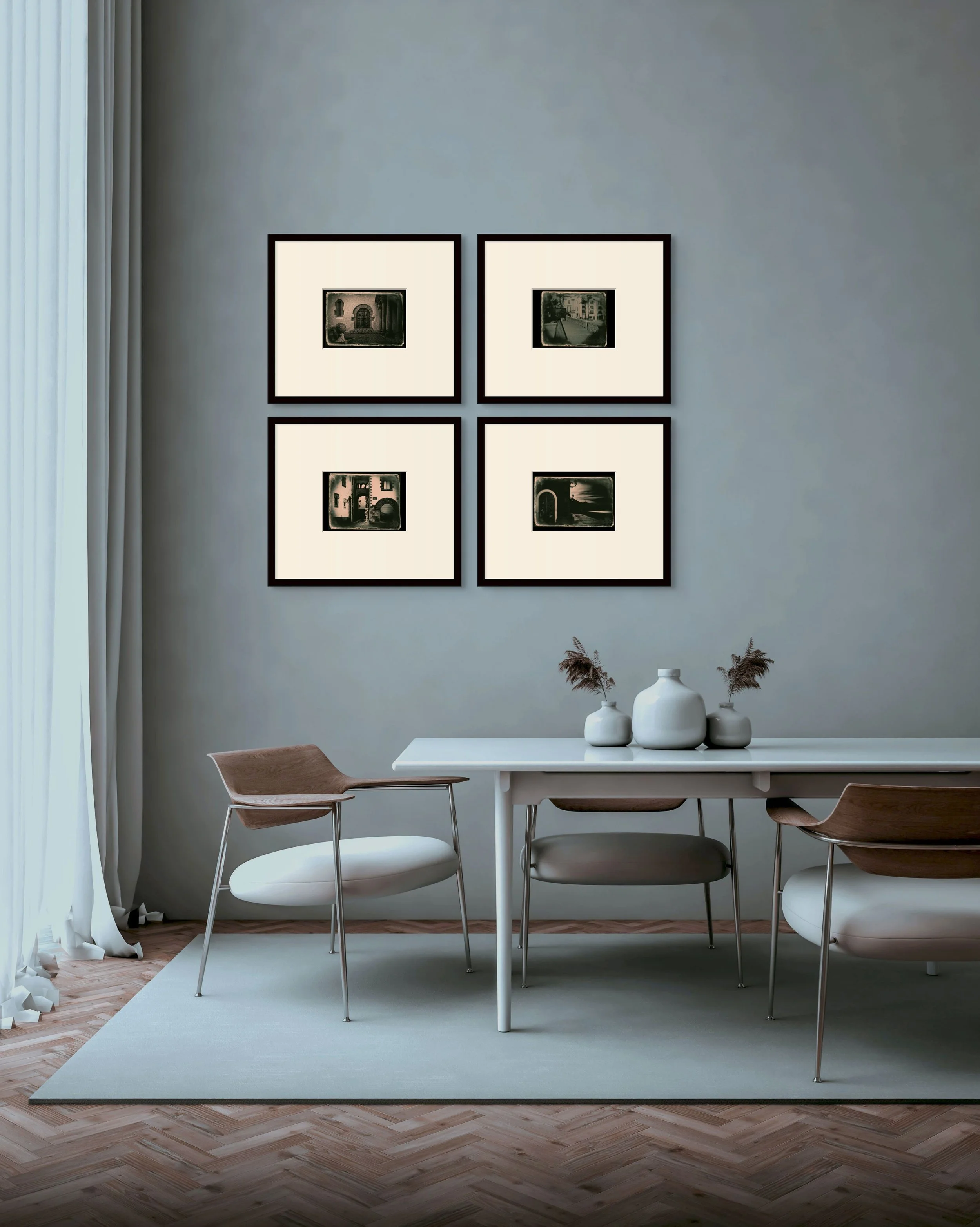 A modern dining room features a white table with three chairs, white vases with dried plants, a light-colored rug, and four framed black-and-white photographs on a light gray wall.