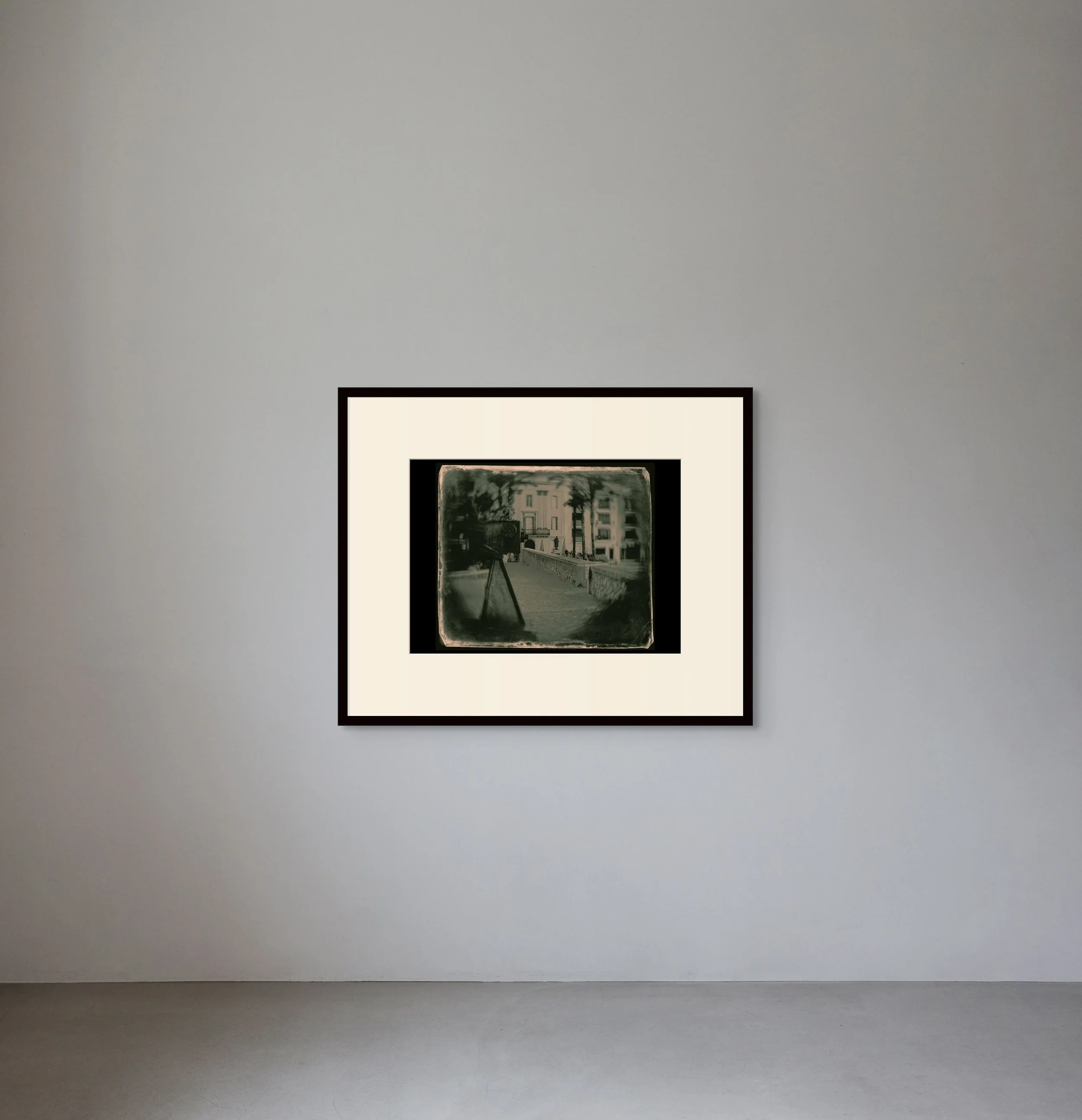 Framed black-and-white photograph of an urban street scene hanging on a plain, light-colored gallery wall.