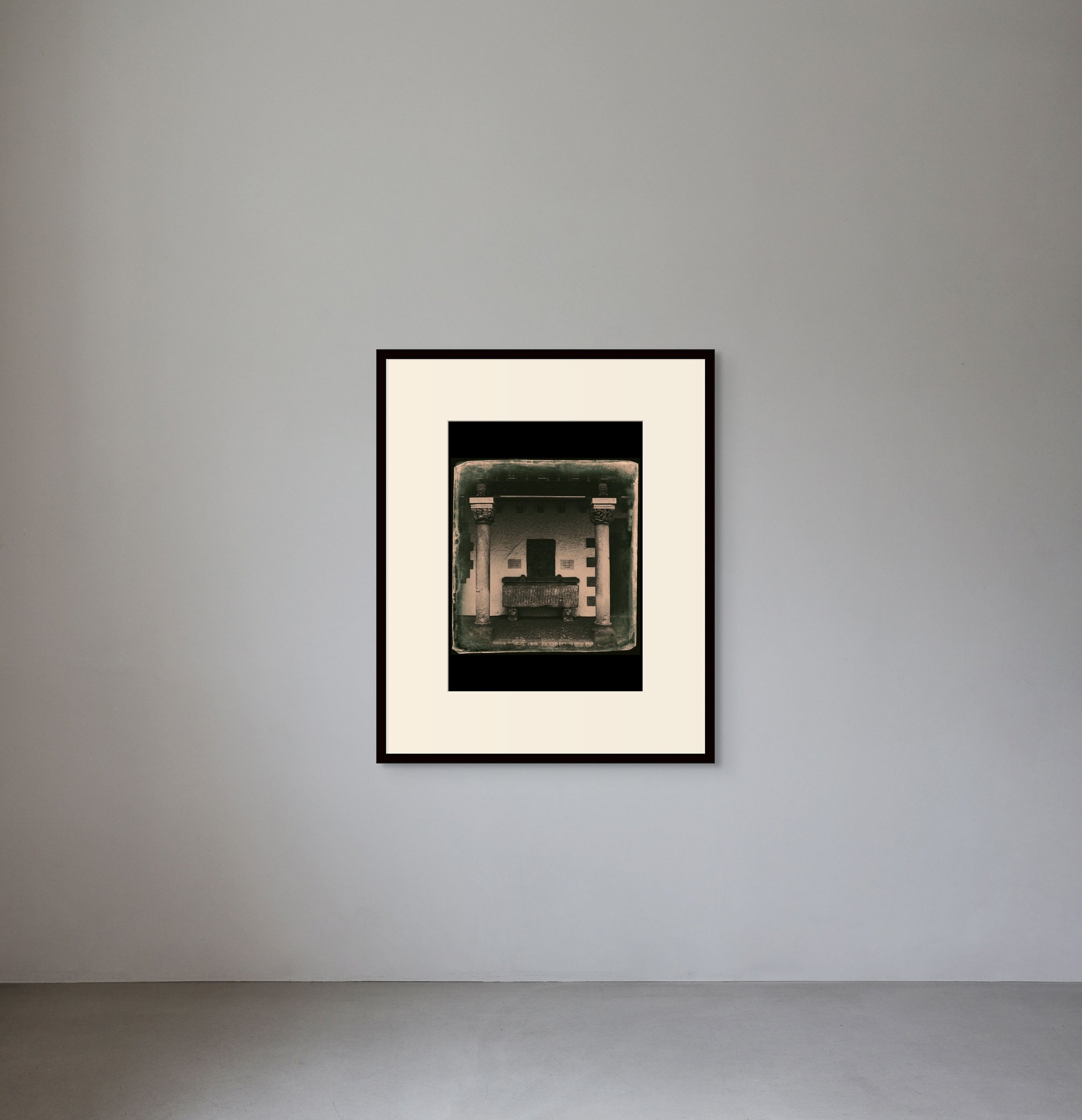 A framed black and white artwork hung on a plain white wall in an art gallery or museum.