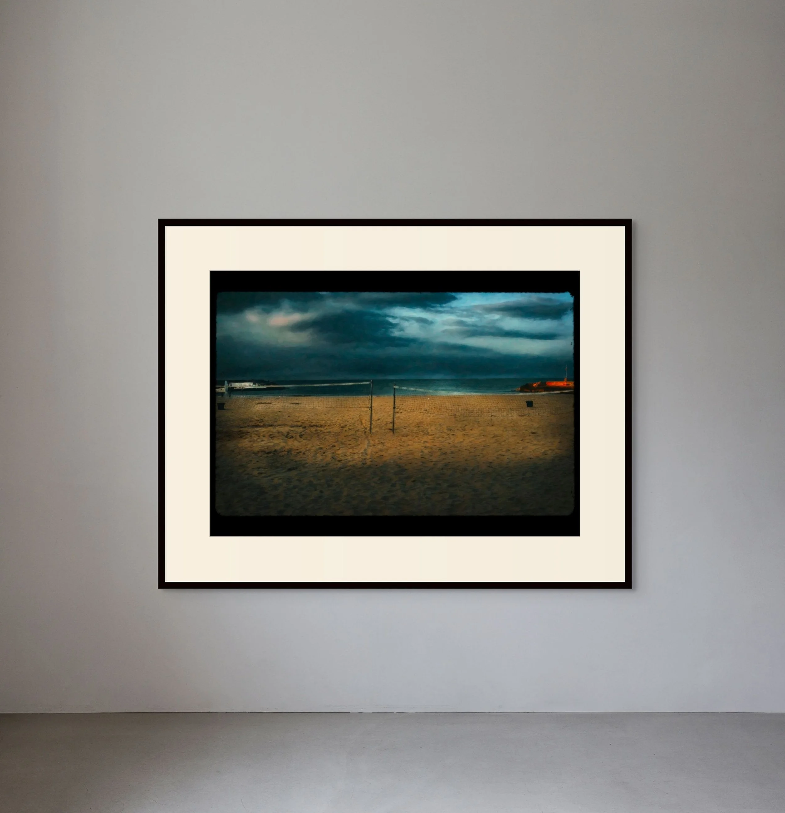 Photograph of a sandy beach with a volleyball net, dark stormy clouds in the sky, and the ocean in the background.
