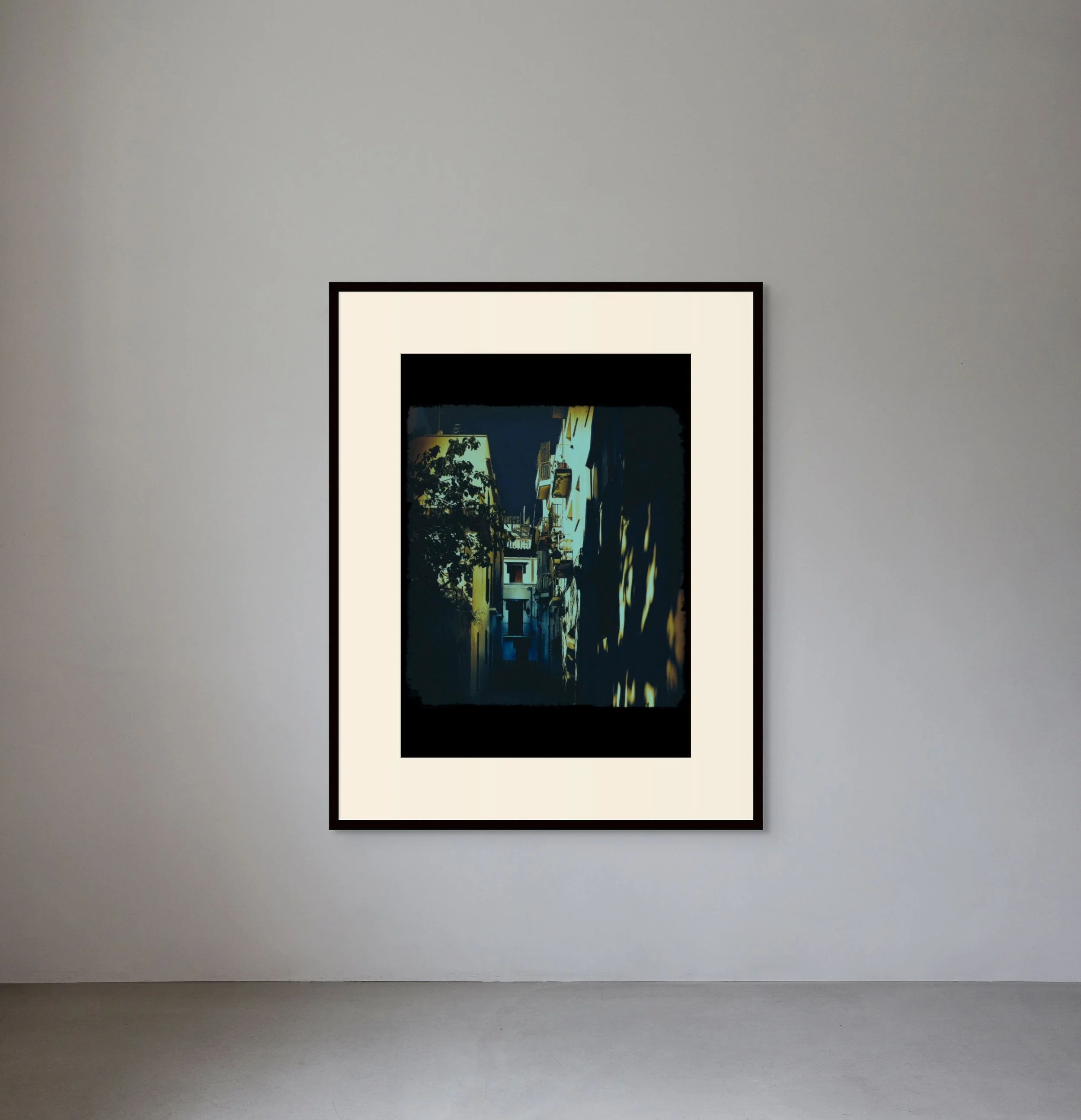 A framed digital art print of a street scene at night hangs on a plain white gallery wall.