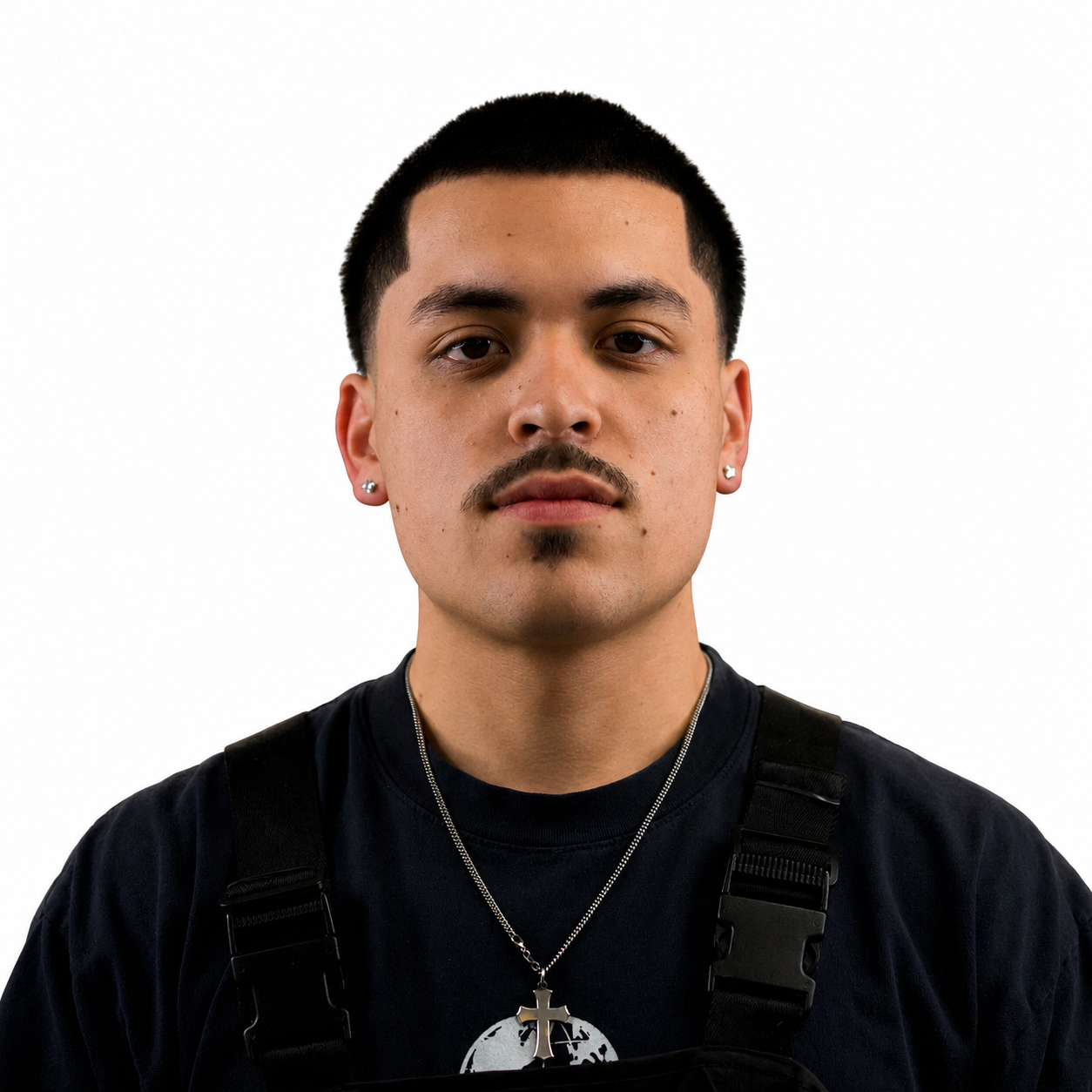 Joseph Quiñones- A barber with short hair and a mustache, wearing a dark shirt and necklace, standing in a dimly lit room with reflective surfaces.