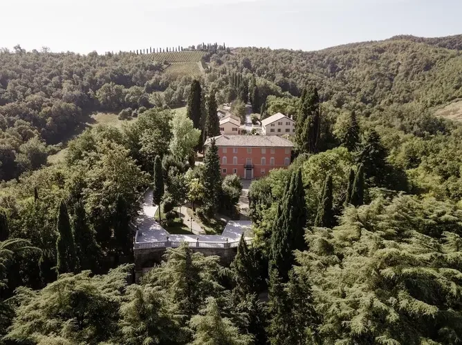 Birds eye view of a terra cotta color winery estate among a green forest and vineyards