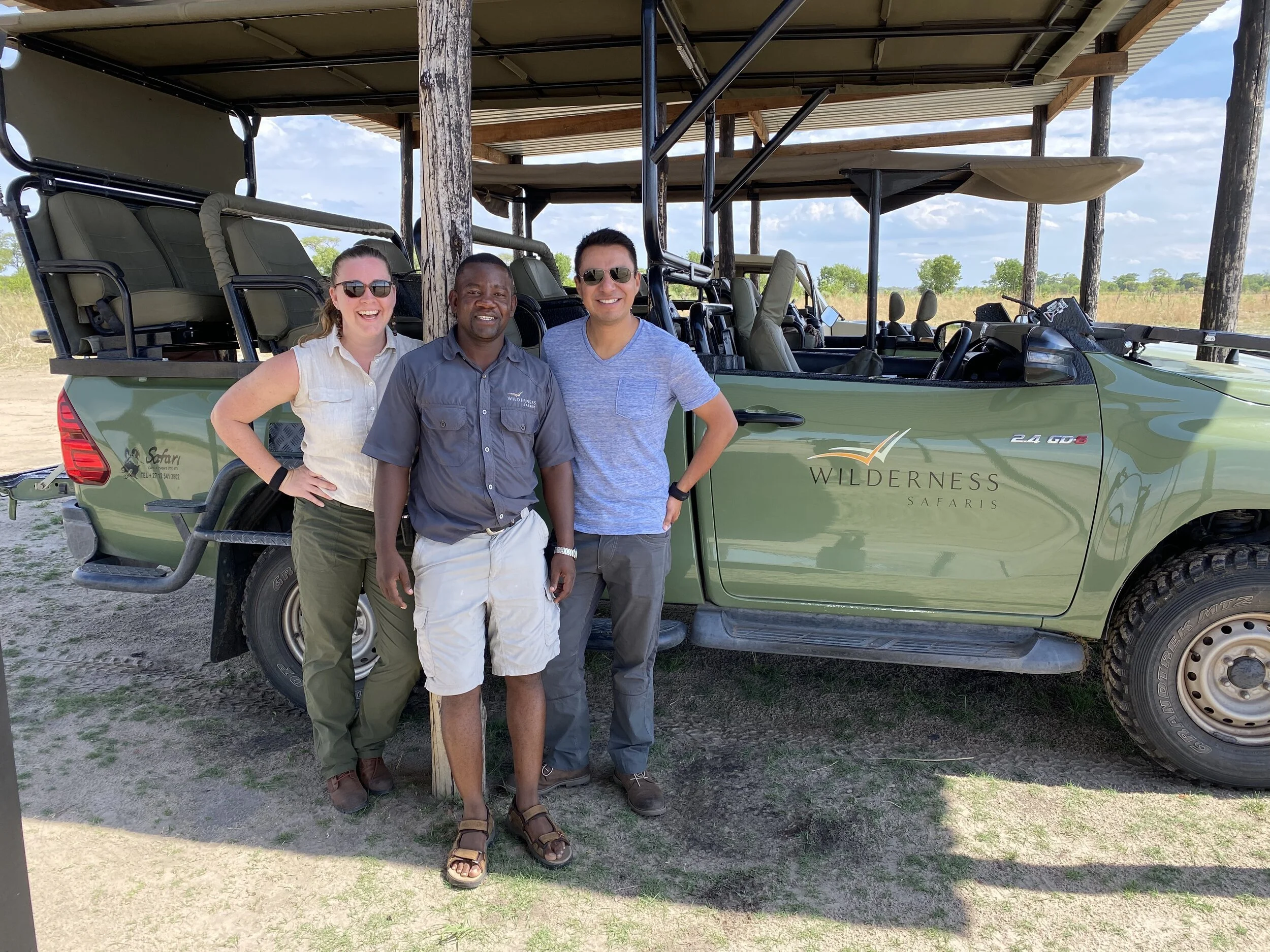 a traveling couple smiles with a guide in Botswana in front of a safari truck