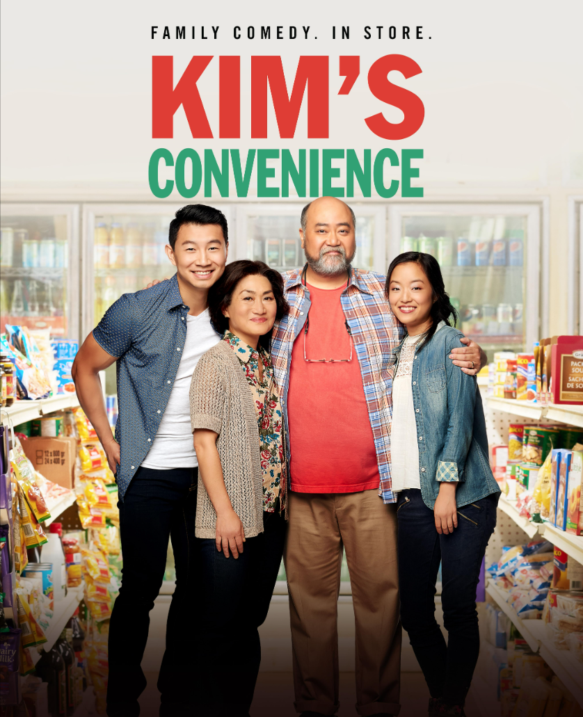 Four family members standing together inside a grocery store aisle, smiling, with shelves of snacks and food behind them. The image promotes a show called 'Kim's Convenience' with the tagline 'Family comedy. In store.'