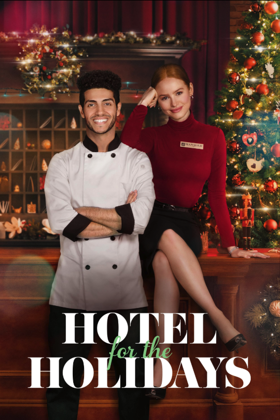 A smiling male chef in a white uniform standing with arms crossed and a female hotel staff in a red sweater and black skirt sitting on a wooden counter, with Christmas decorations and a lit Christmas tree in the background.