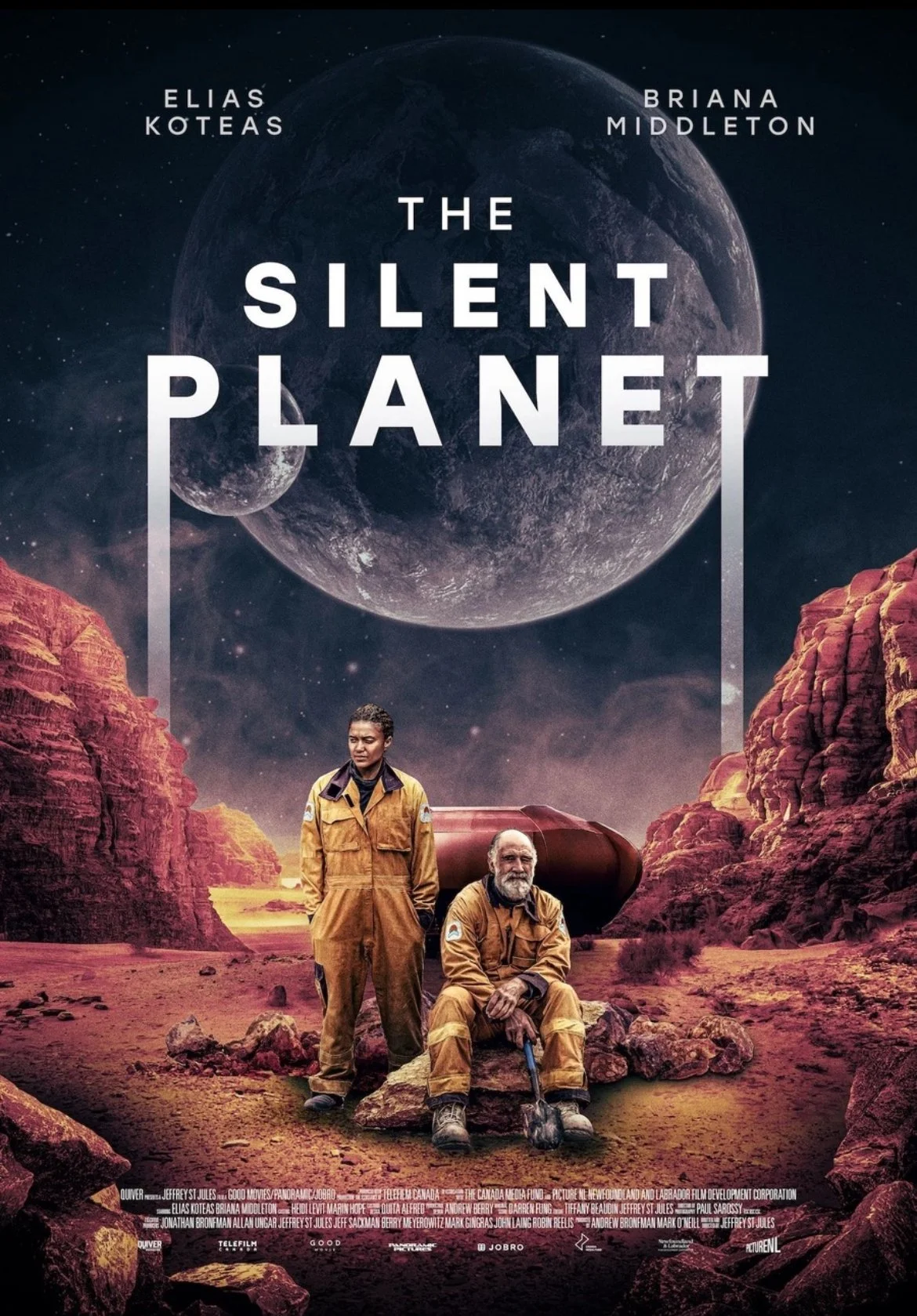 Movie poster for 'The Silent Planet' featuring two astronauts in orange suits on a barren, rocky landscape with large red rock formations, and a cosmic background with a large moon or planet and smaller celestial bodies.