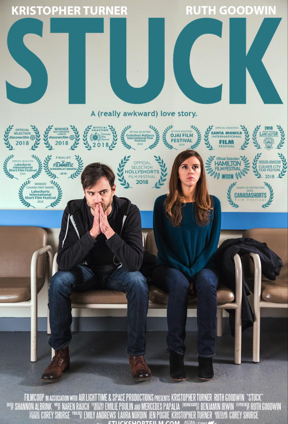 A man with dark hair and a woman with long hair sit on a row of chairs in a waiting area, with their hands clasped in front of their mouths, appearing worried. Behind them, a poster promoting the film "Stuck" features laurels and awards from film fes