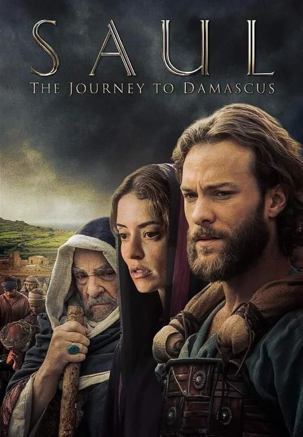 Movie poster for 'Saul: The Journey to Damascus' featuring a man with a beard and long hair, a woman, and an elderly man in a hooded cloak, set against a background of a landscape with hills and a cloudy sky.
