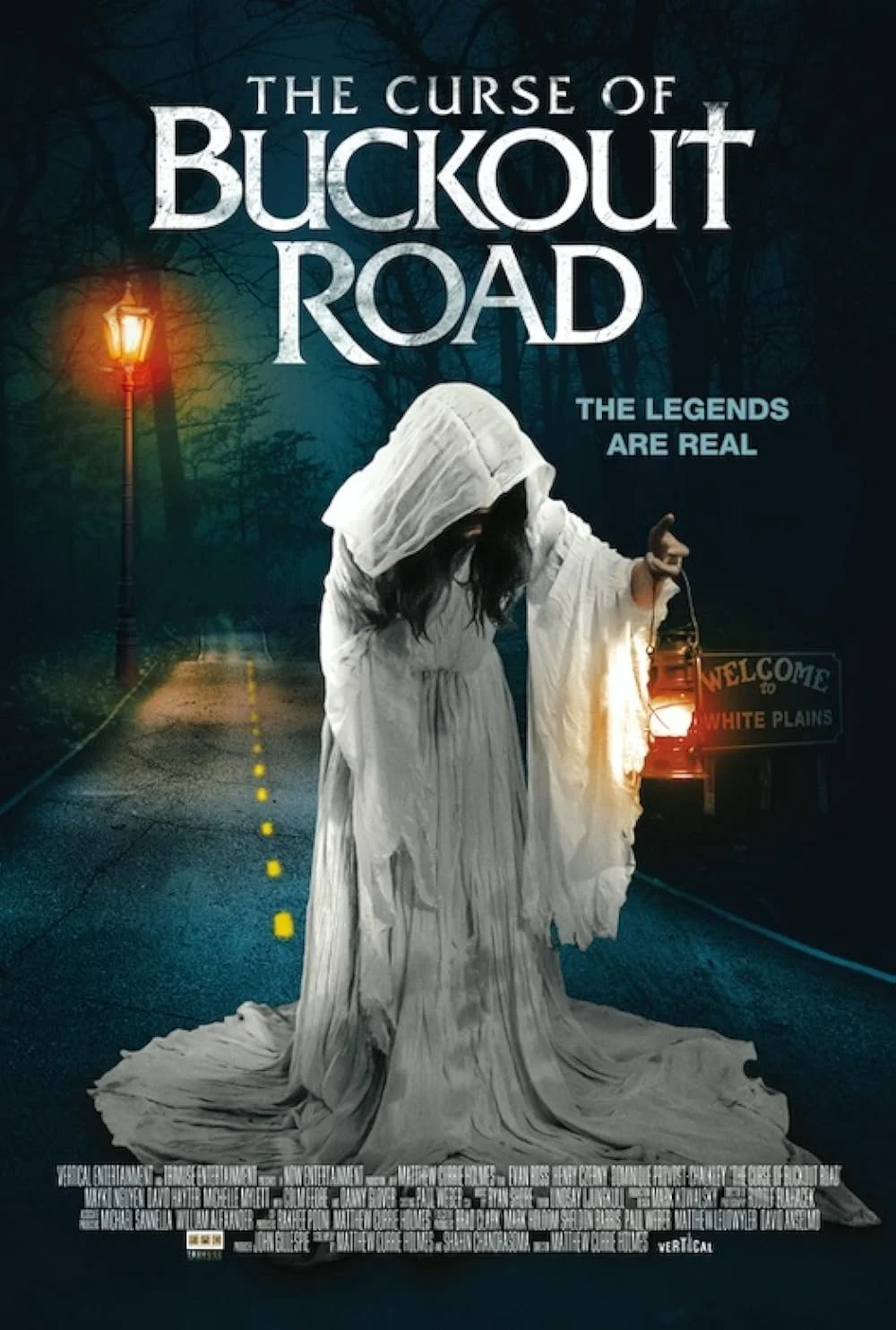 Movie poster for 'The Curse of Buckout Road' featuring a ghostly figure in a white dress holding a lantern, standing on an empty dark road at night with a streetlamp and welcome sign in the background.