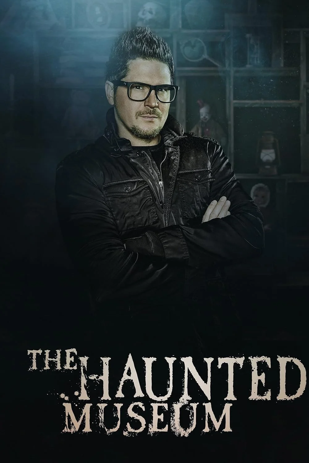 A man with glasses and a goatee, wearing a black leather jacket, stands with arms crossed in front of a dark background with haunted house decorations, and the text "The Haunted Museum" at the bottom.