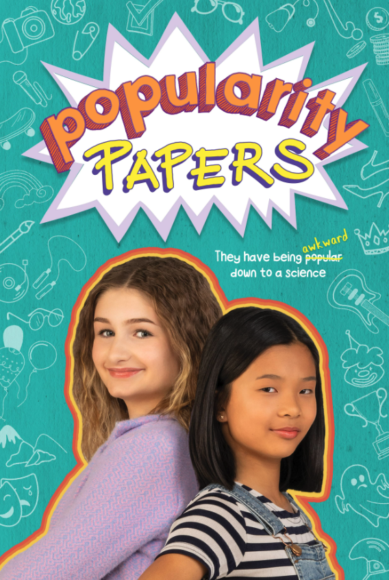Cover of a magazine titled "Popularity Papers" featuring two girls, one with wavy blonde hair wearing a lavender shirt and the other with straight black hair wearing a striped shirt and overalls, standing back to back. The background is teal with whi