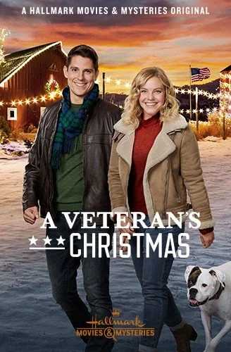 A man and woman smiling, standing outside with a dog, in front of a barn decorated with Christmas lights and American flags, during sunset, promotional poster for a Hallmark movie titled 'A Veteran's Christmas'.