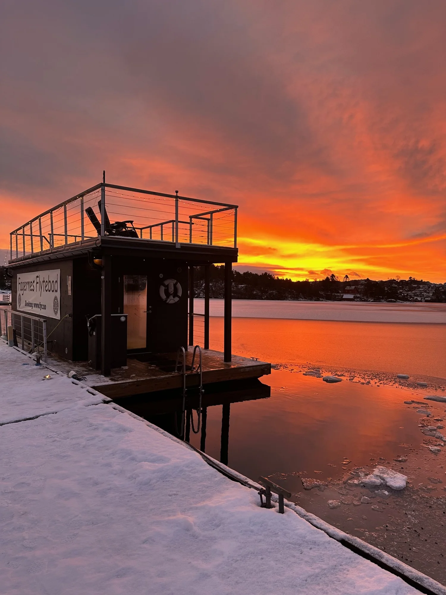 Fagernes floating sauna beside a snowy deck and orange sunset reflected across the lake.