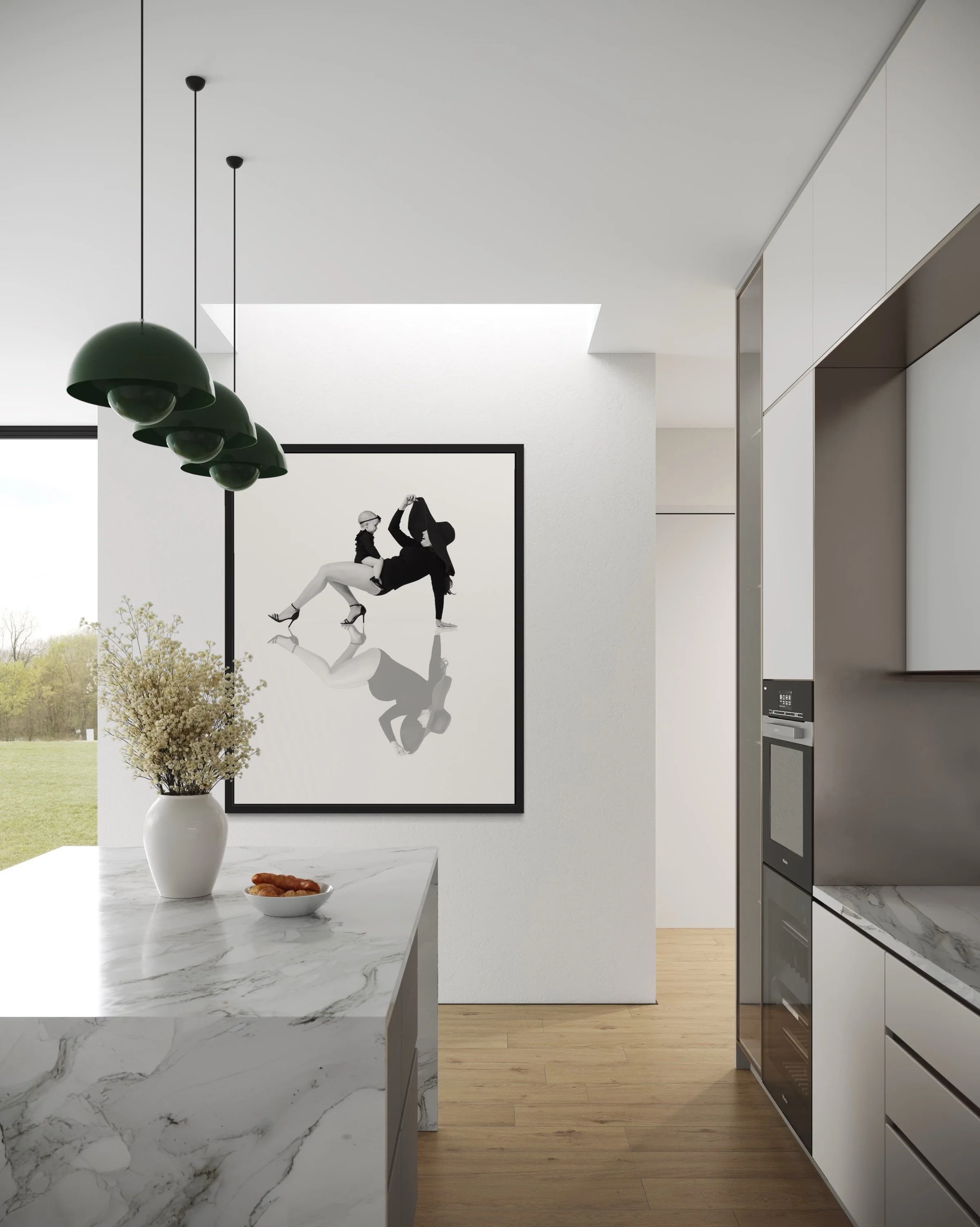 Modern kitchen with marble island, black and white artwork of two women dancing, green pendant lights, vase with flowers, and a view of a grassy landscape outside.