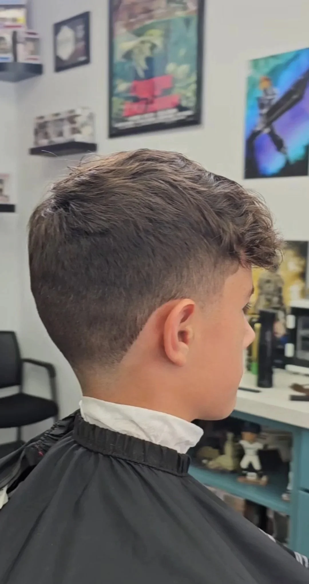 Side view of a young man with a fresh haircut in a barbershop, with framed posters on the wall in the background.
