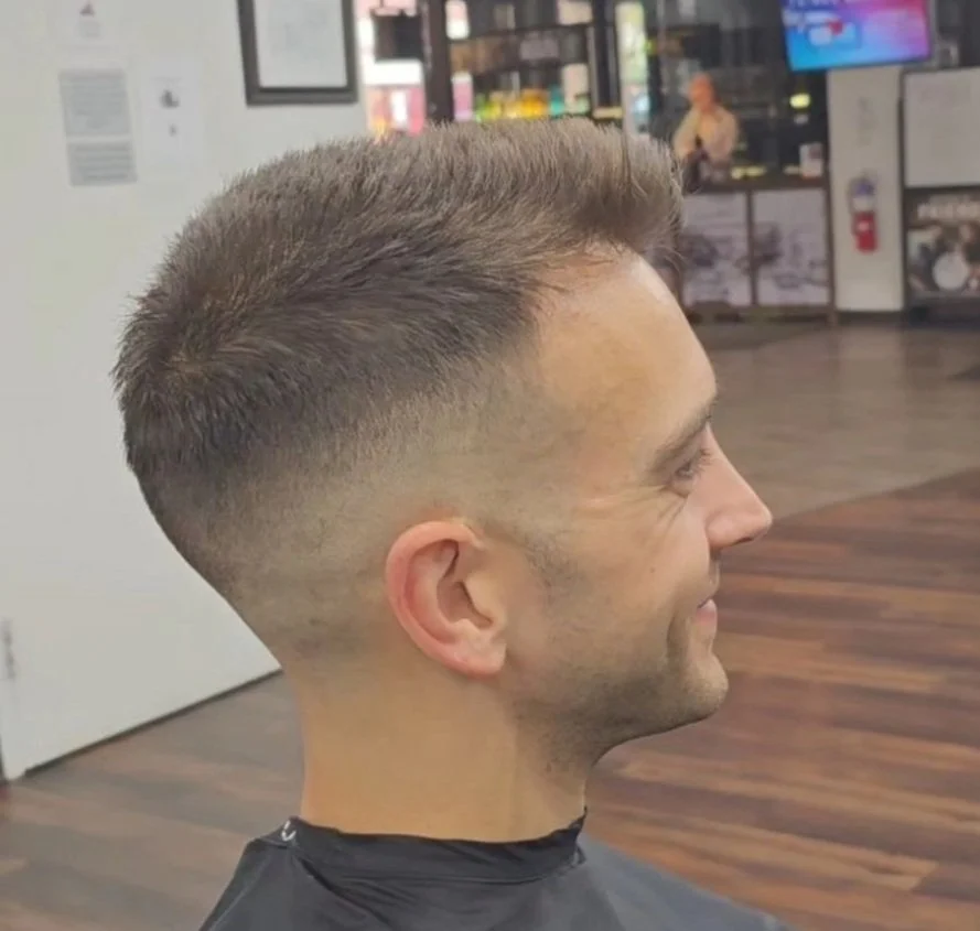 Side profile of a man with a fresh, faded haircut in a barbershop.