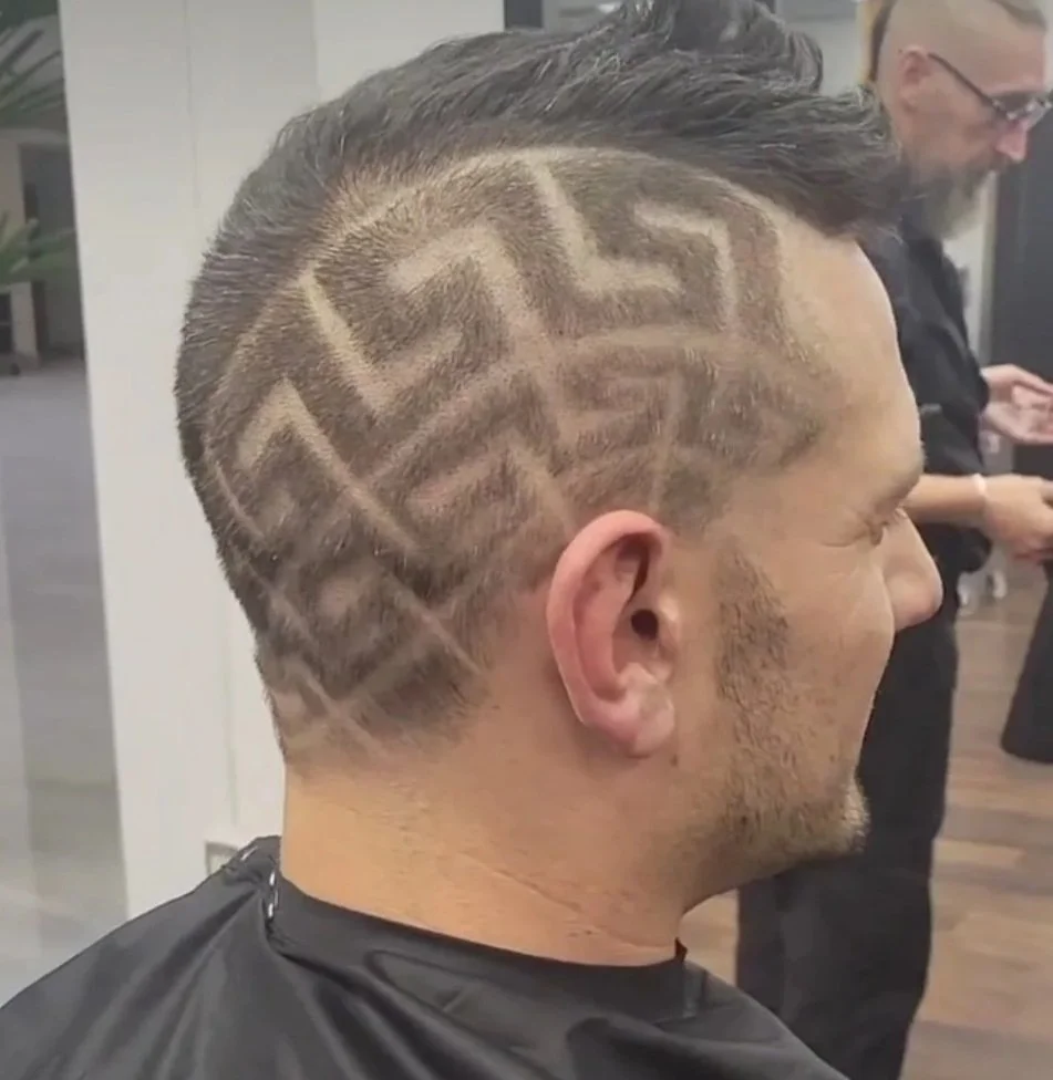 Side view of a man with a haircut featuring a geometric pattern shaved into the sides of his head.
