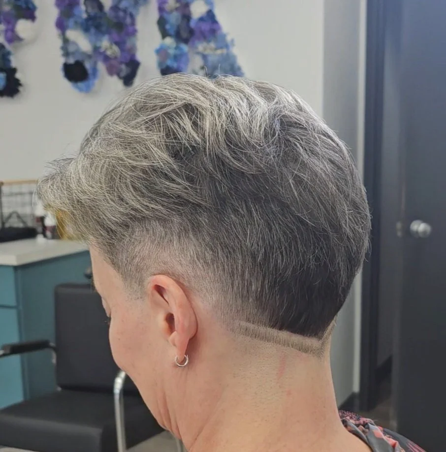 A woman with short, gray hair featuring a stylish fade haircut with a design shaved into the back of the neck.