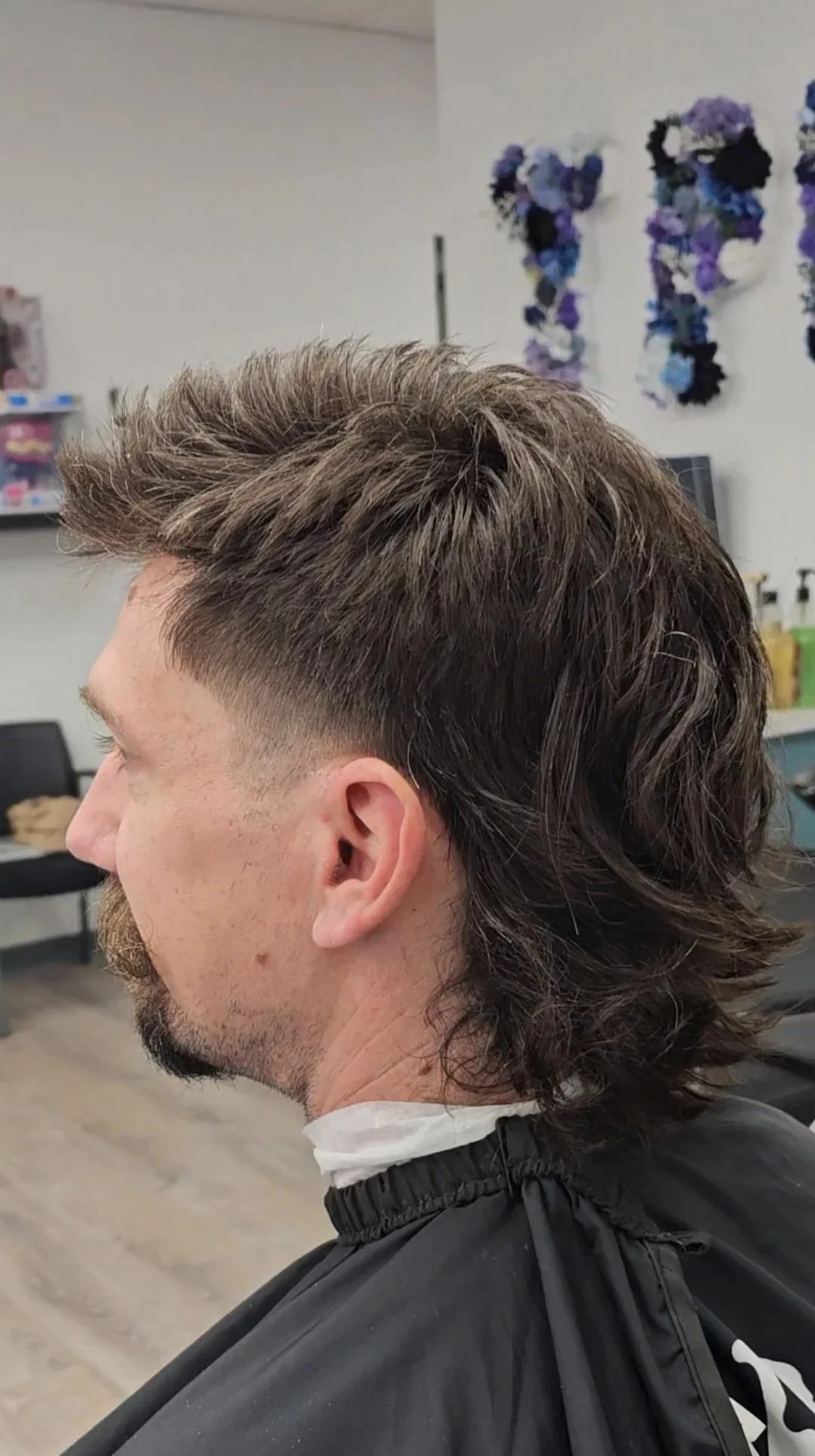 Side view of a man with a new haircut featuring a fading undercut and longer, textured hair on top, seated in a barbershop.