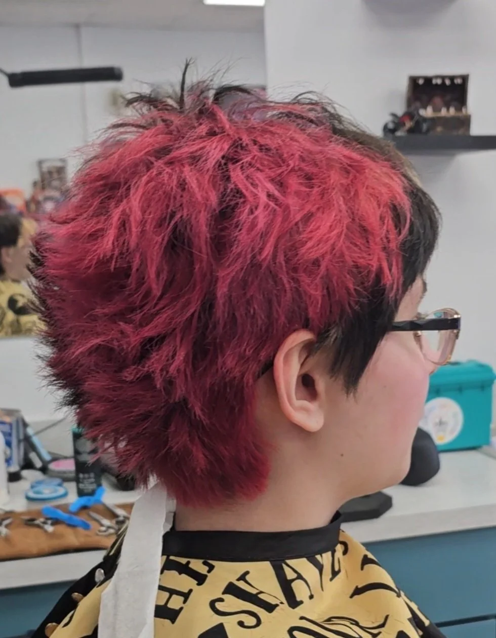 Hair styled in a short, choppy cut with a vibrant red color on top, fading into black at the sides, in a salon setting.