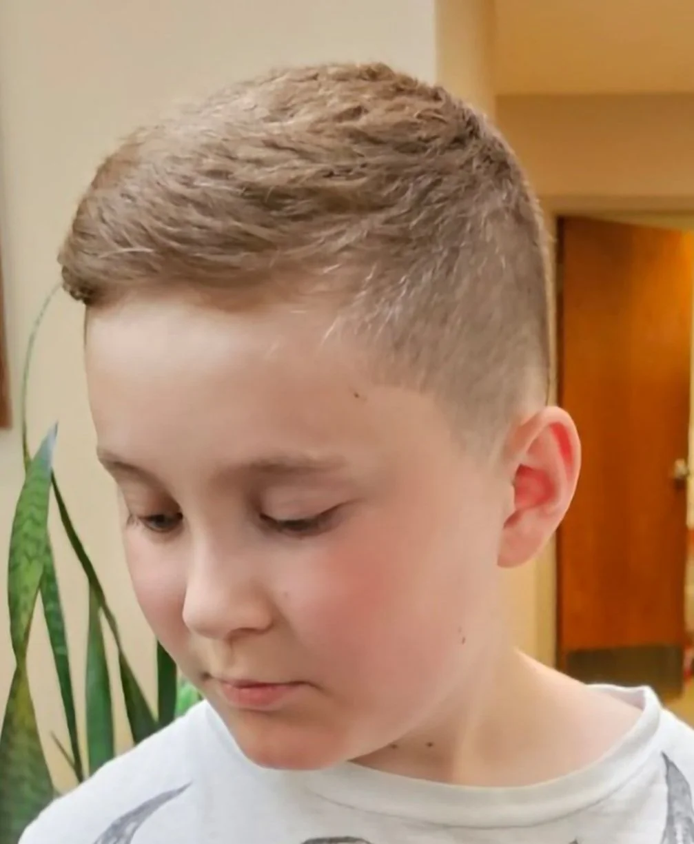 Close-up of a young boy with a short, textured hairstyle in an indoor setting.