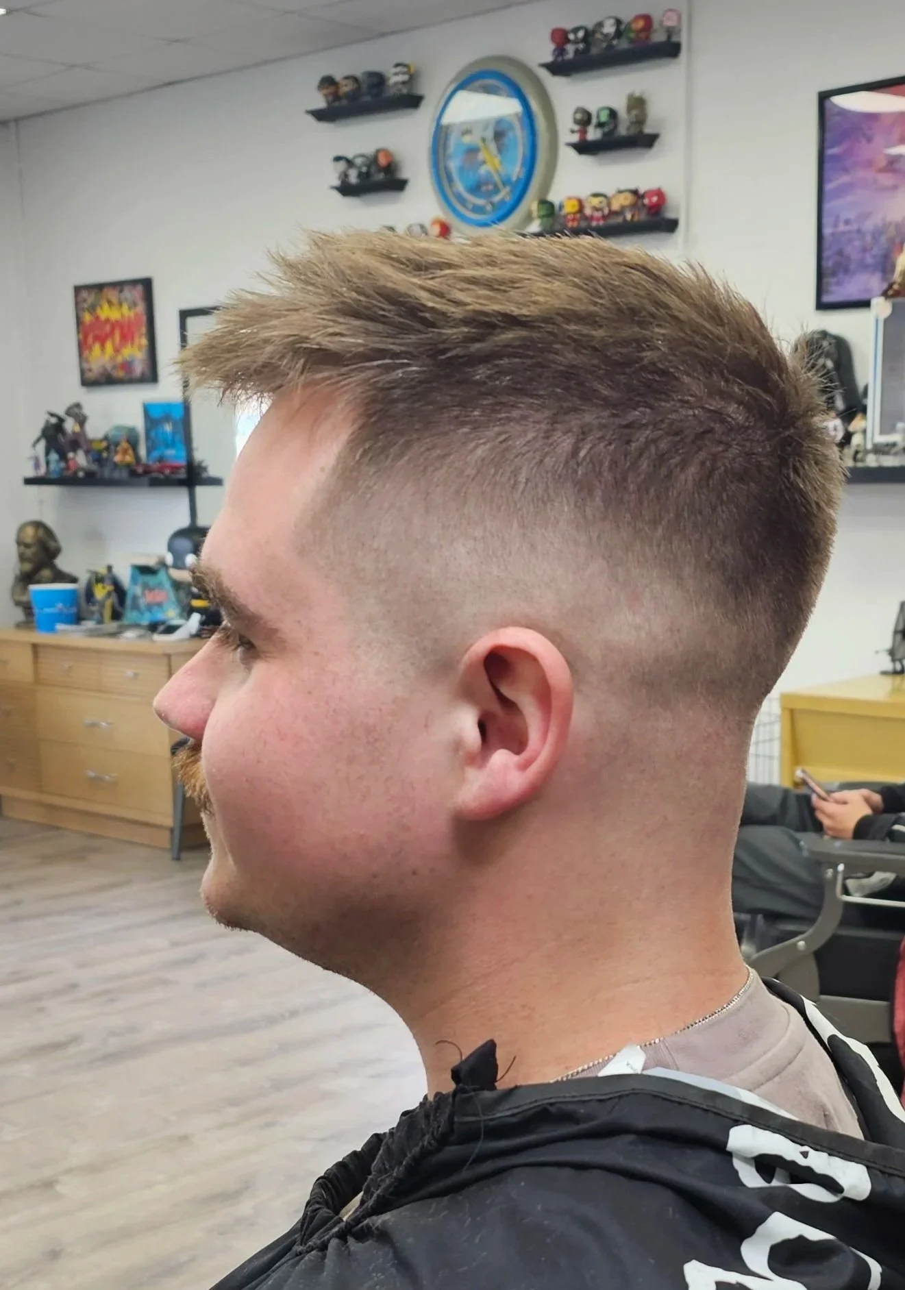 Side view of a young man with a fresh haircut, with fade sides and longer textured hair on top, sitting in a barbershop.