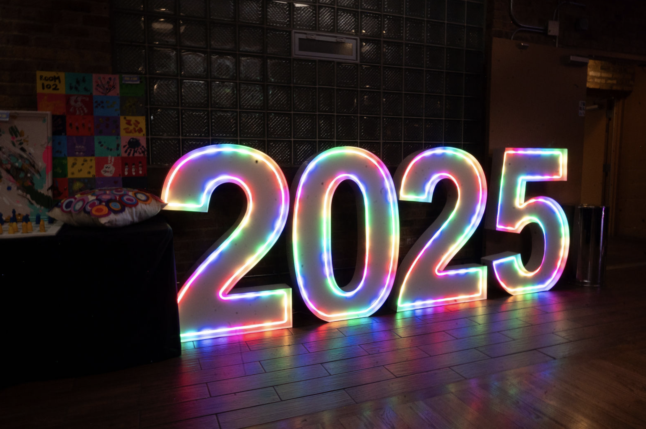 Neon-lit illuminated numbers displaying '2025' in a colorful glow at an indoor event.
