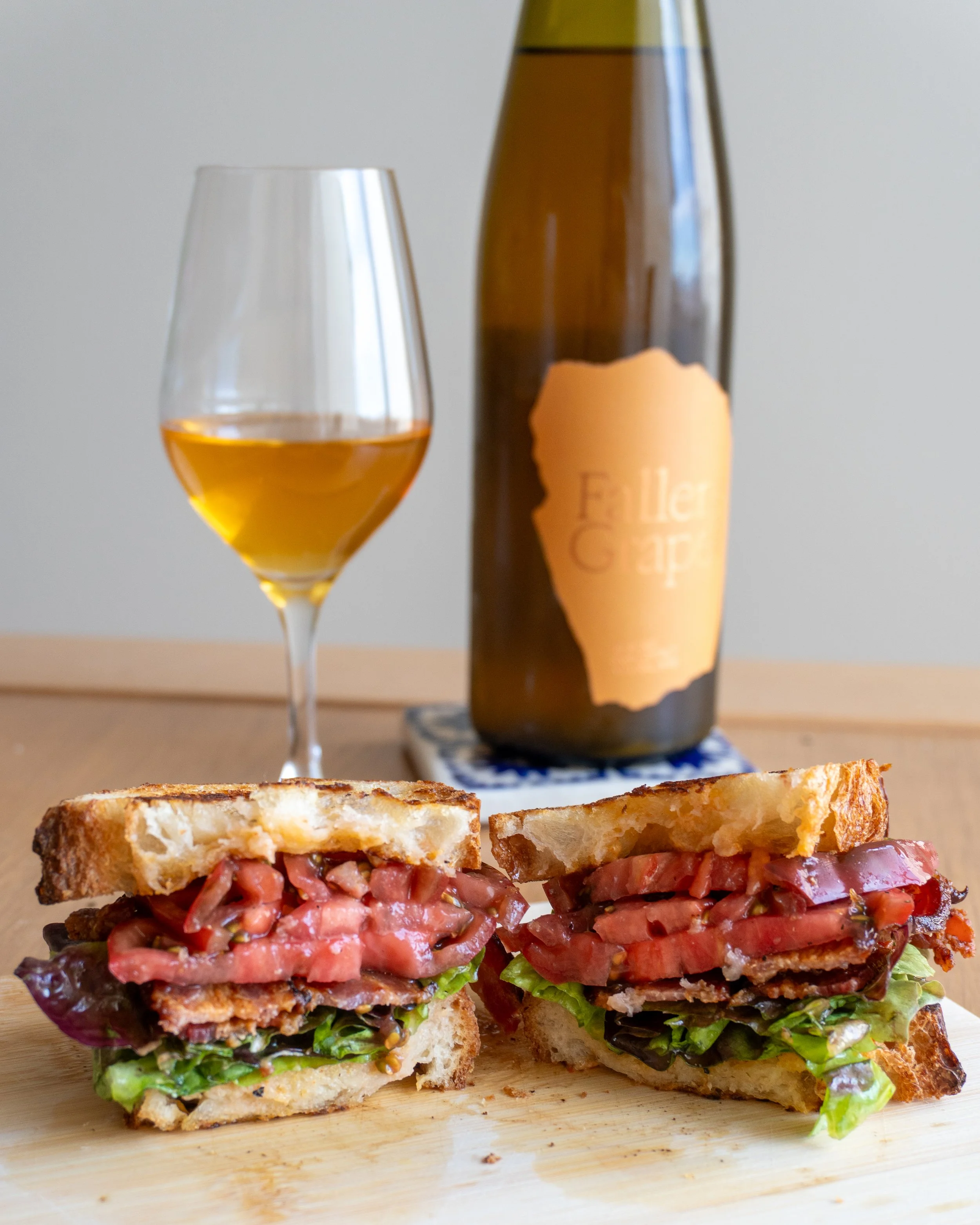 Close-up of BLT sandwich with toasted bread, lettuce, bacon, and thick layers of tomato, set on a wooden cutting board.