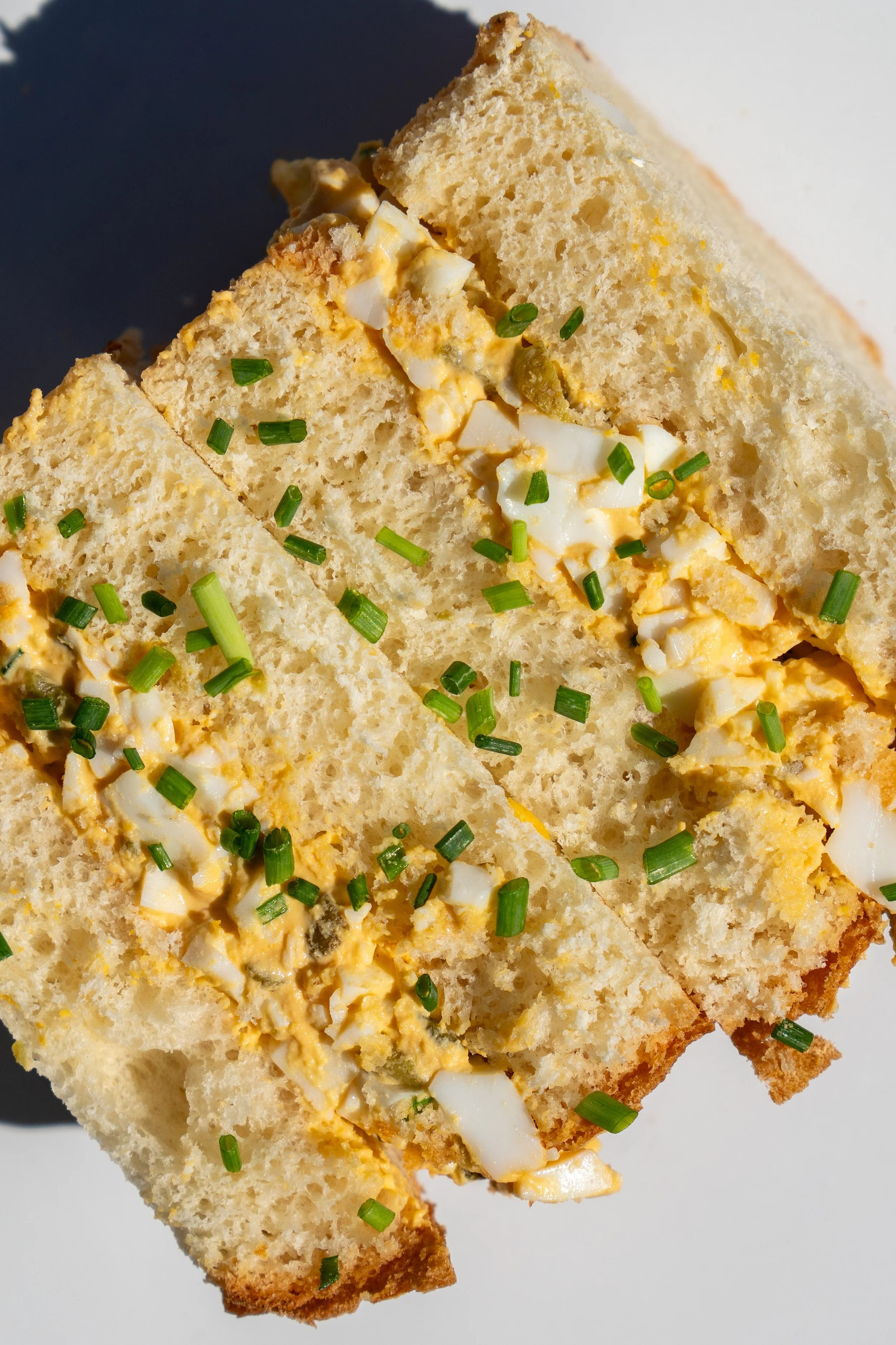 A slice of egg salad sandwich garnished with chopped green onions, showing a creamy mixture of chopped eggs and mayonnaise between slices of bread.