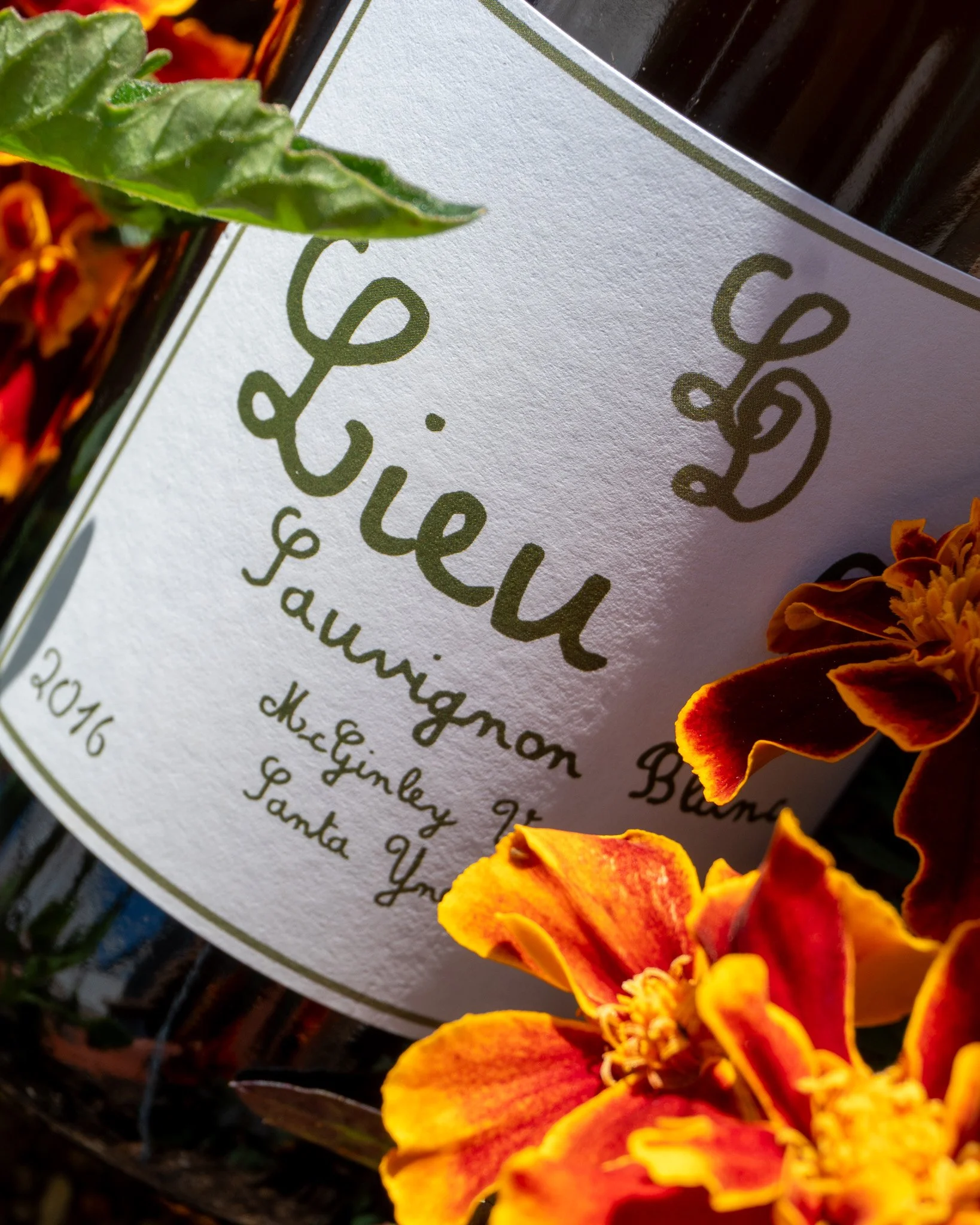 Close-up of a label on a bottle with green font, surrounded by orange and red marigold flowers.