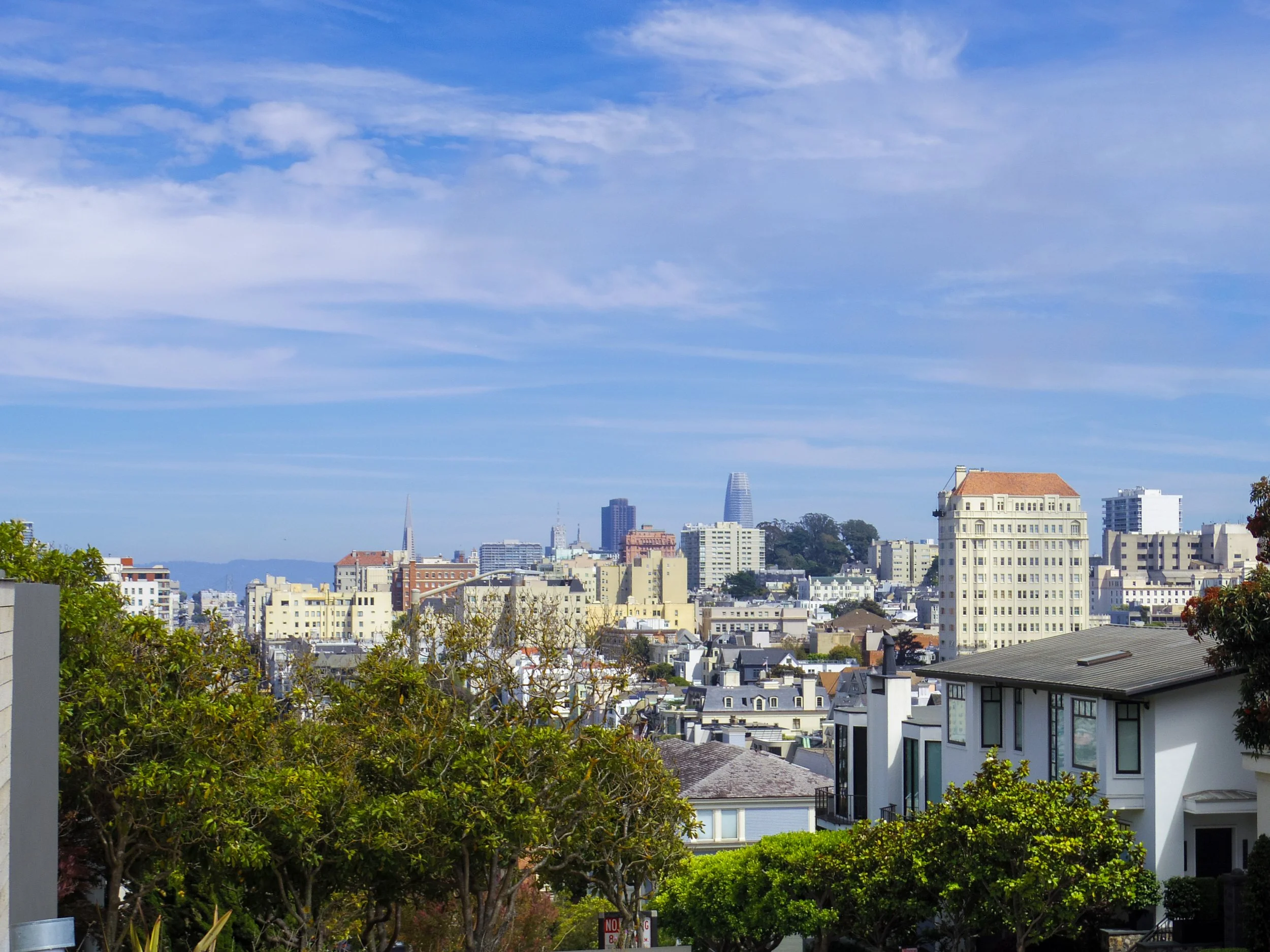 The San Francisco skyline against a clear blue sky with wispy white clouds.