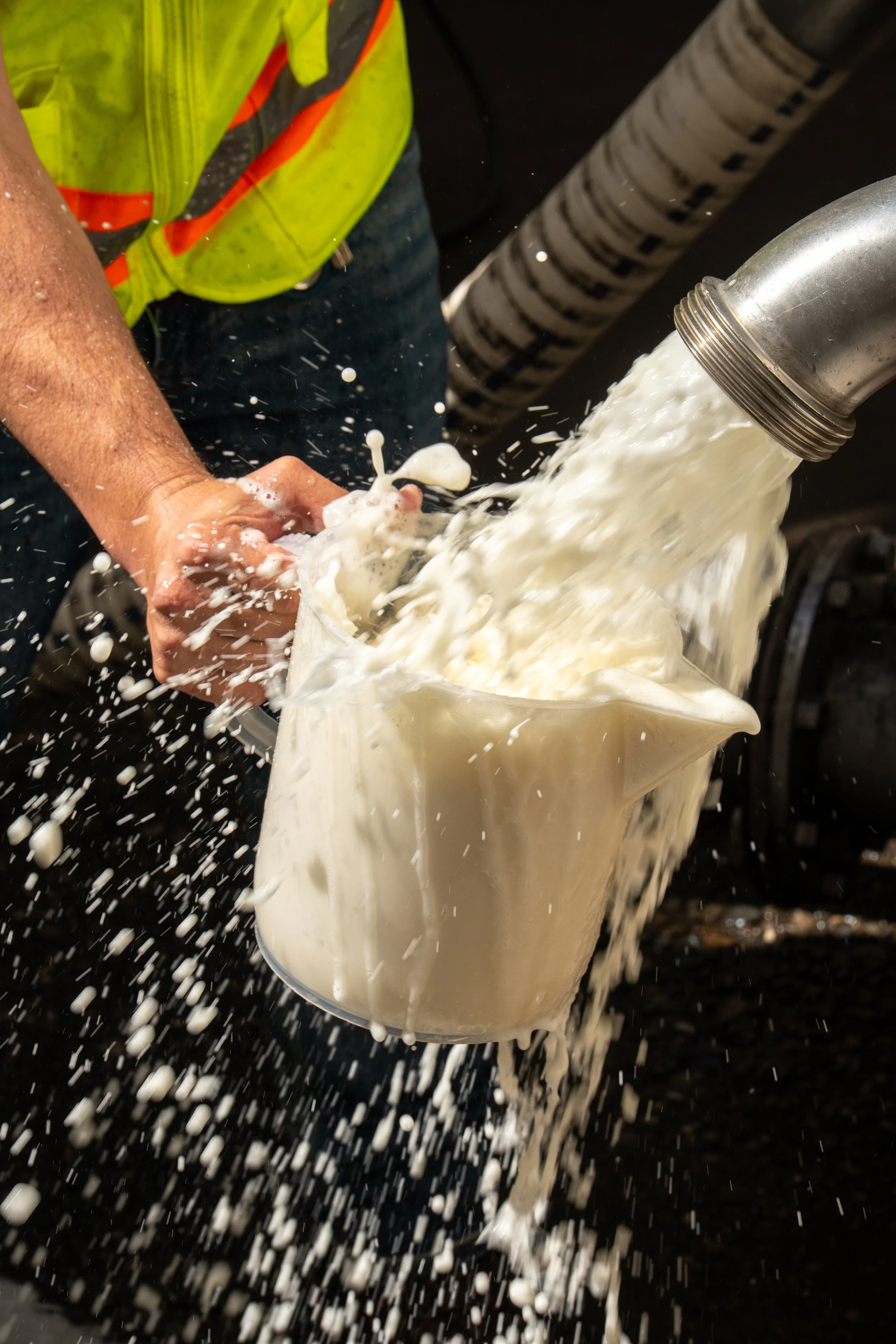 Worker wearing a high-visibility jacket catches a stream of fermenting wine.