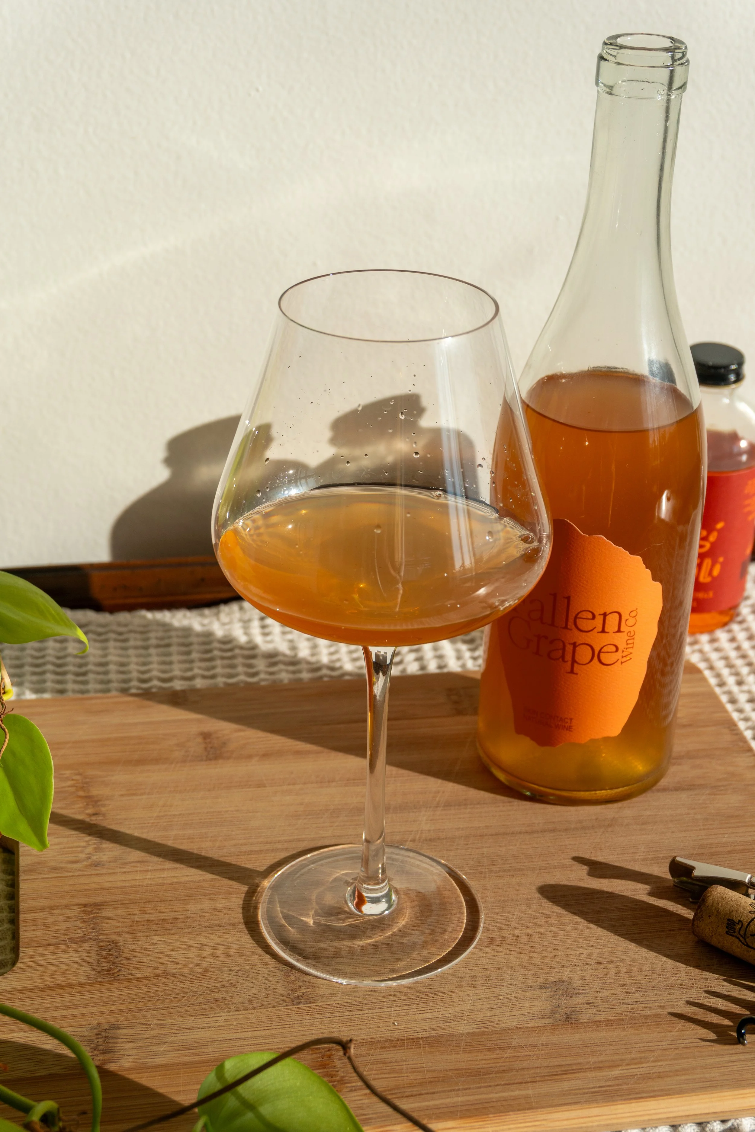 A glass of orange wine on a wooden table with a wine bottle in the background.