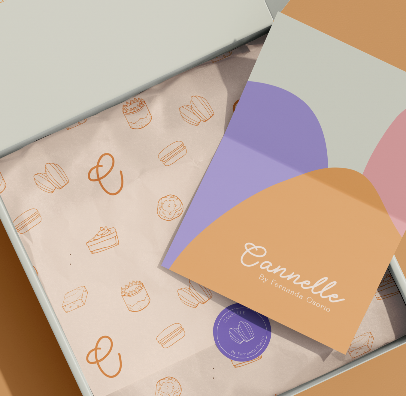 Caja de regalo abierta con papel decorativo de postres y un papel de colores con el texto "Cannelle By Fernanda Osorio".
