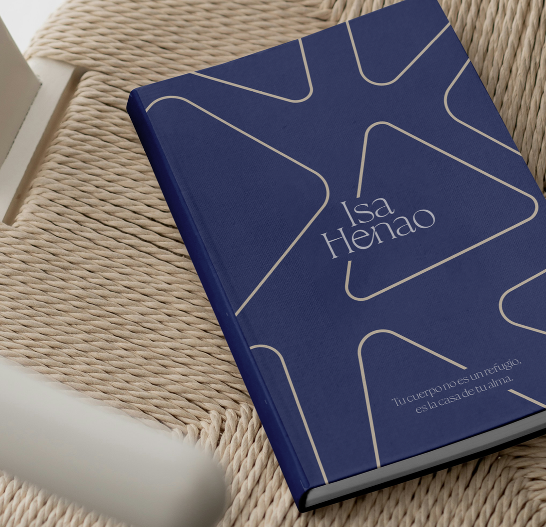 Libro azul con diseño geométrico blanco sobre una silla tejida, con el texto "Isa Henao" y una cita en la portada.
