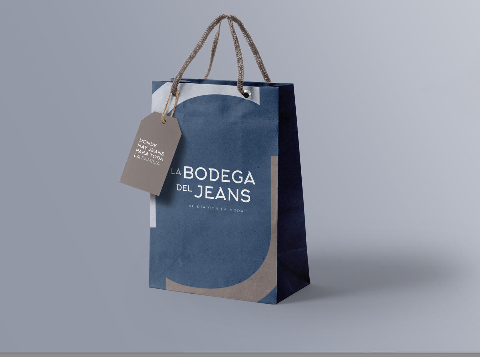 Bolsa de papel azul con asas de cuerda y etiqueta que dice "La Bodega del Jeans" y "Donde hay jeans para toda la familia".