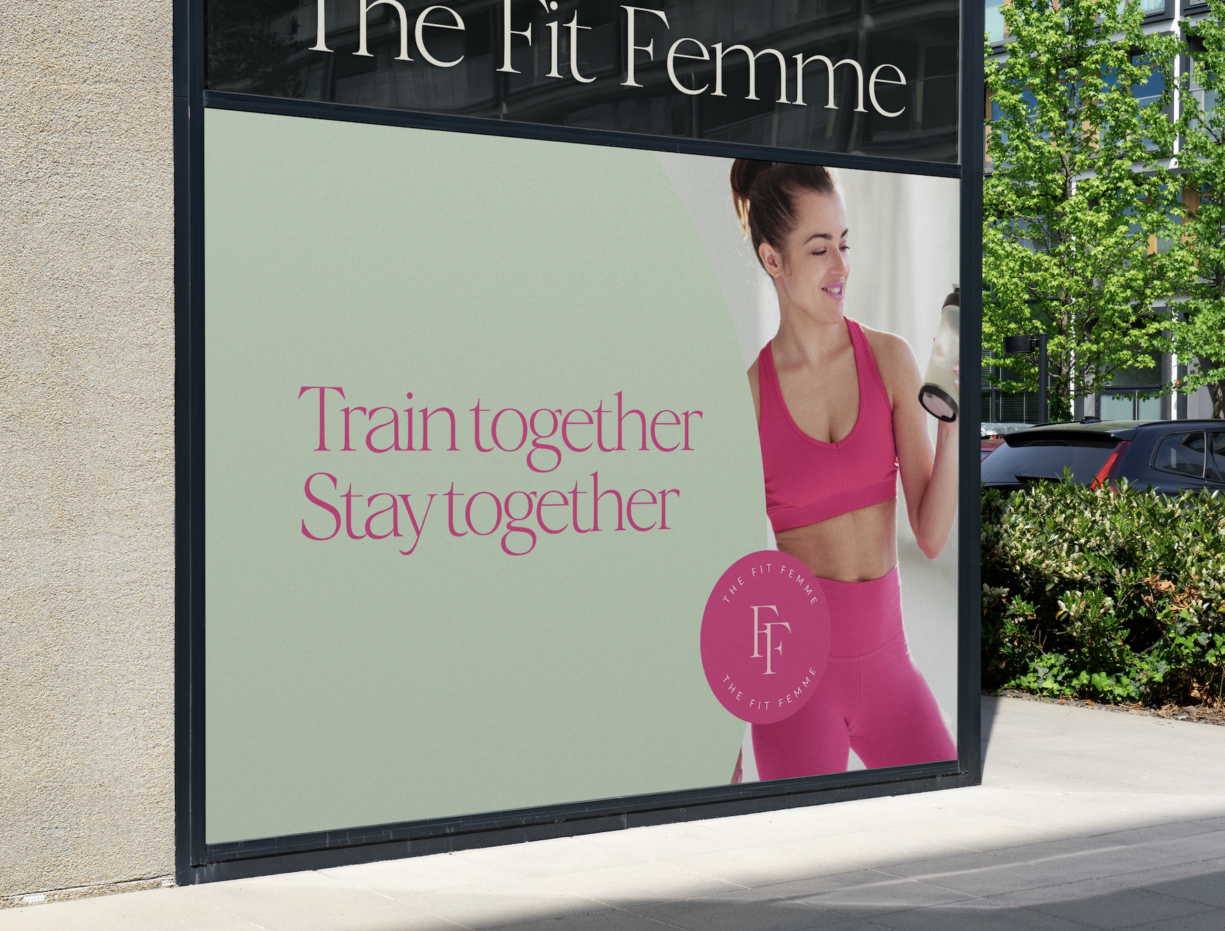 Valla publicitaria de "The Fit Femme" con mujer en ropa deportiva rosa y texto "Train together, Stay together" en inglés.