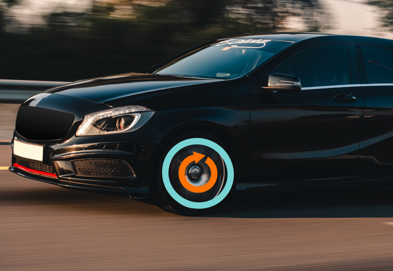 Automóvil negro en movimiento con neumáticos resaltados en azul y naranja. Fondo borroso de carretera y naturaleza.