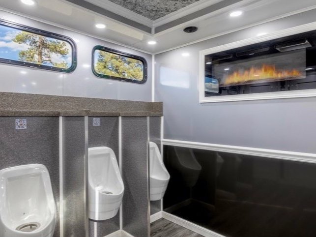 Luxury restroom with three urinals, decorative windows, and a digital fireplace.